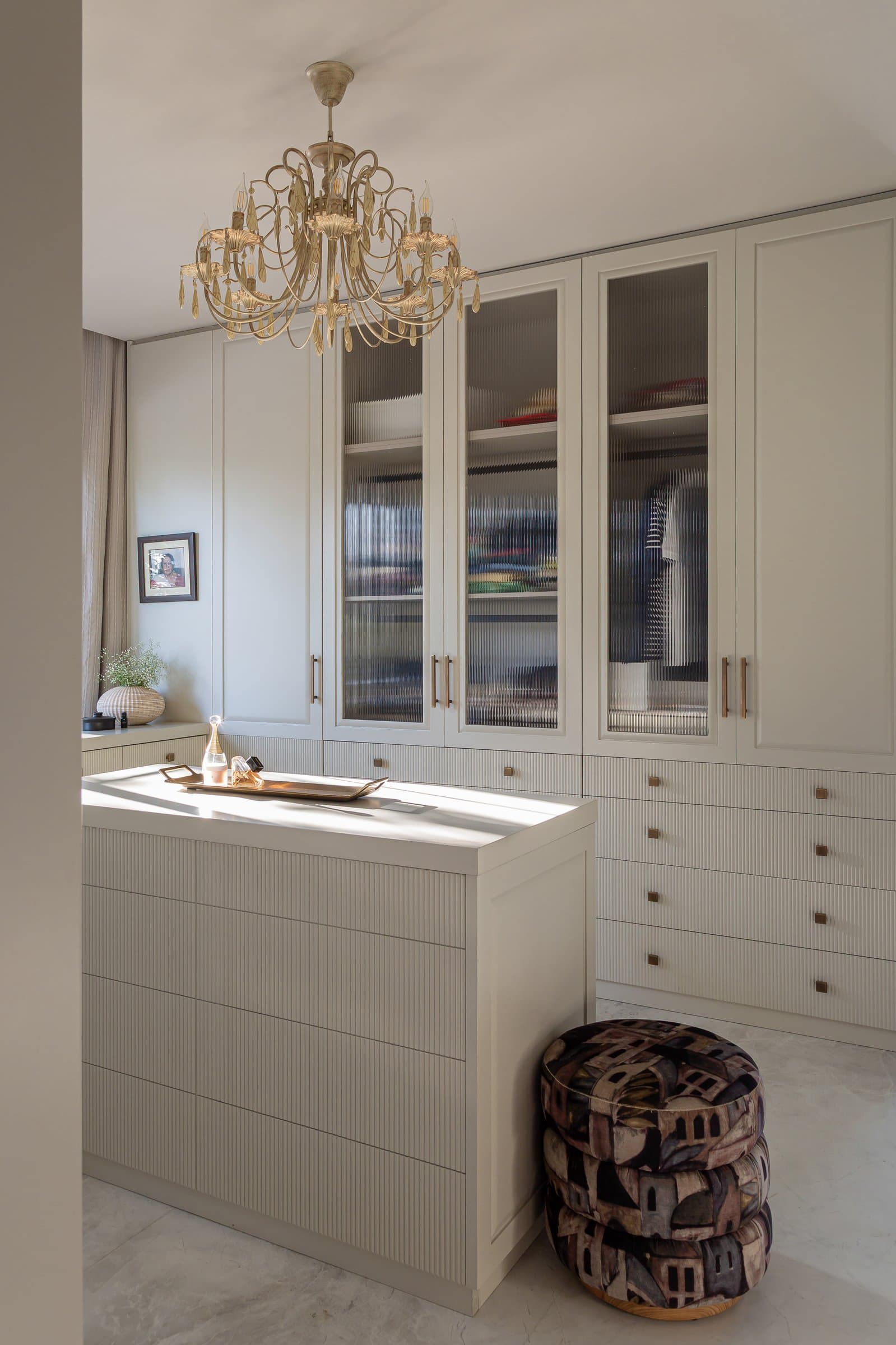 The master dressing room: ivory fluted wardrobes flank a central island, with an aged-brass chandelier suspended above