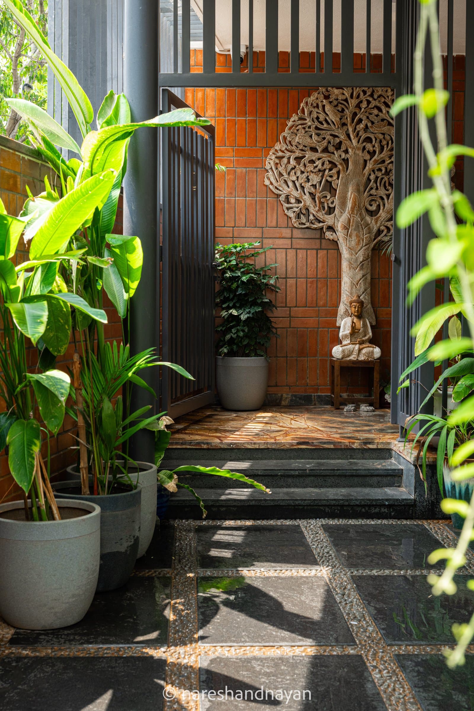 The arrival sequence, with terracotta tiling, a carved tree-of-life panel and a planted edge marking the threshold