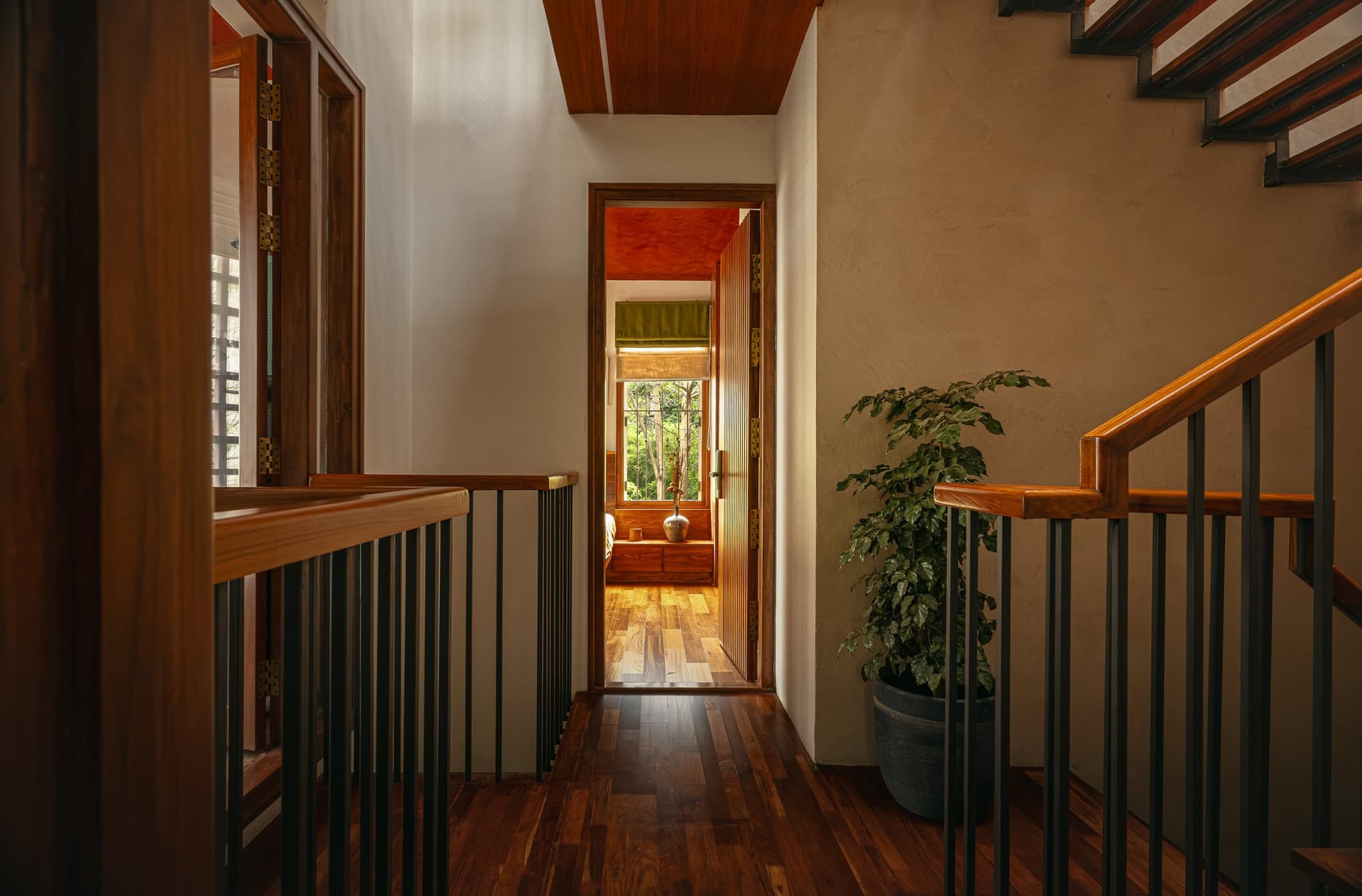 The upper landing, where a planted pot anchors one edge and a slatted hardwood door opens into the bedroom beyond