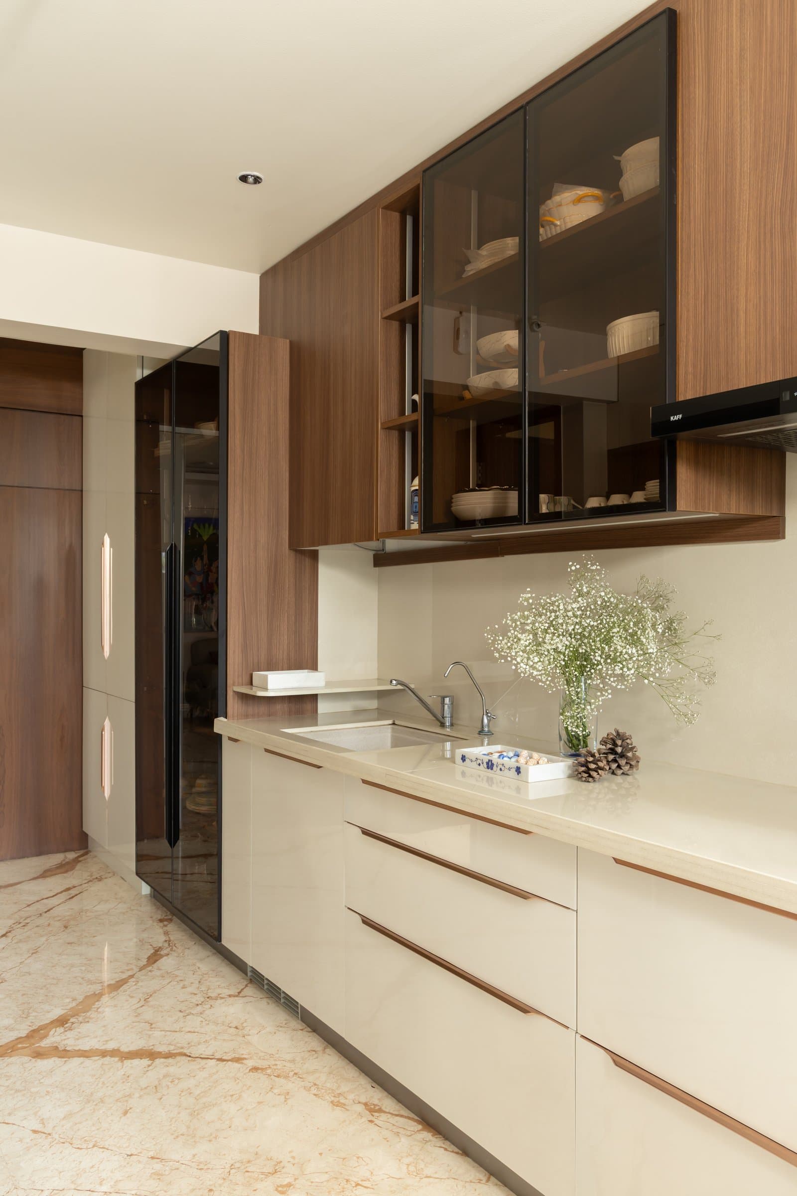 The kitchen, where cream lacquer and walnut-toned cabinetry hold a disciplined galley plan