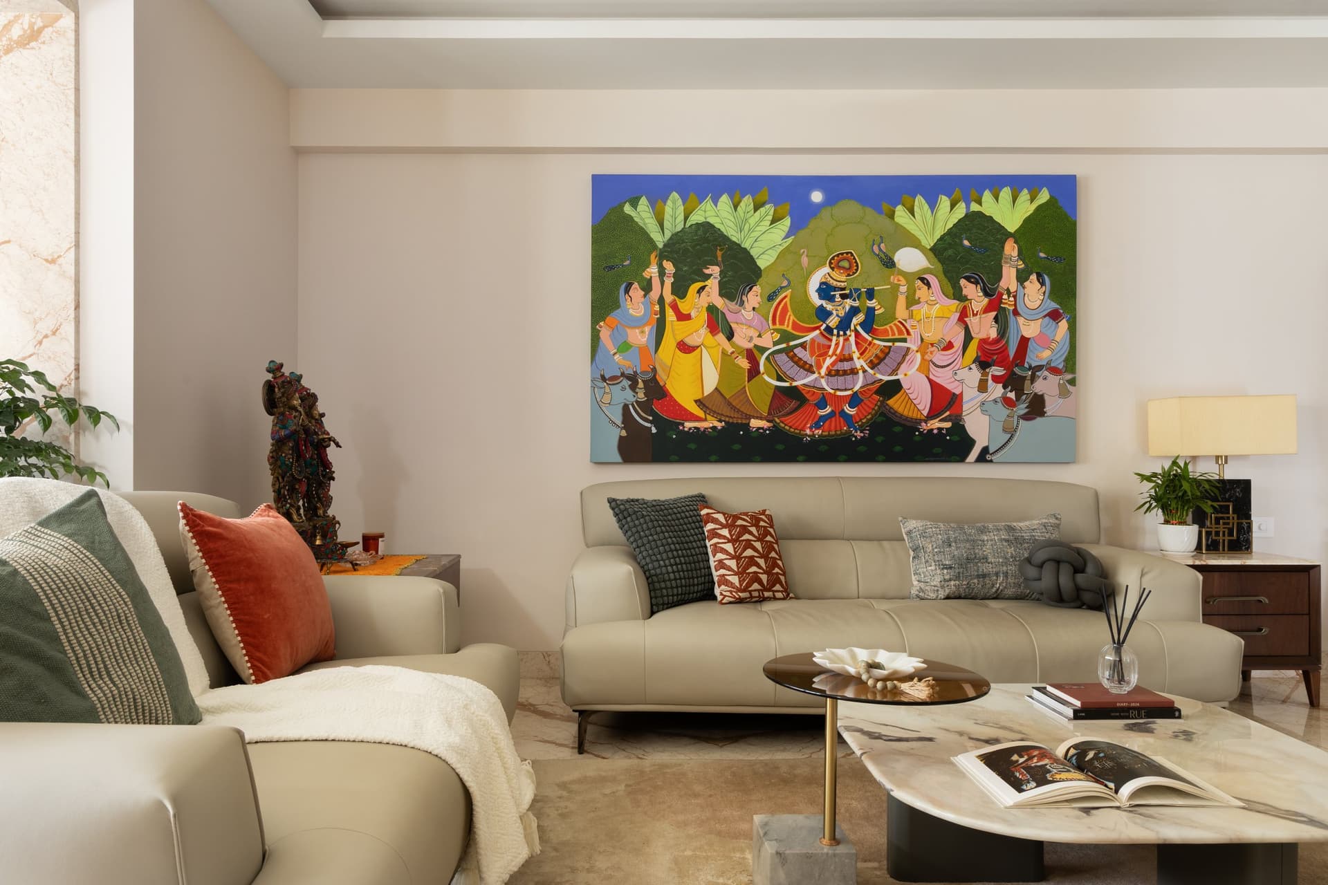 The living room square-on: a low sectional, a small bronze deity at the sofa's edge, and a cushion palette that quietly echoes the painting above
