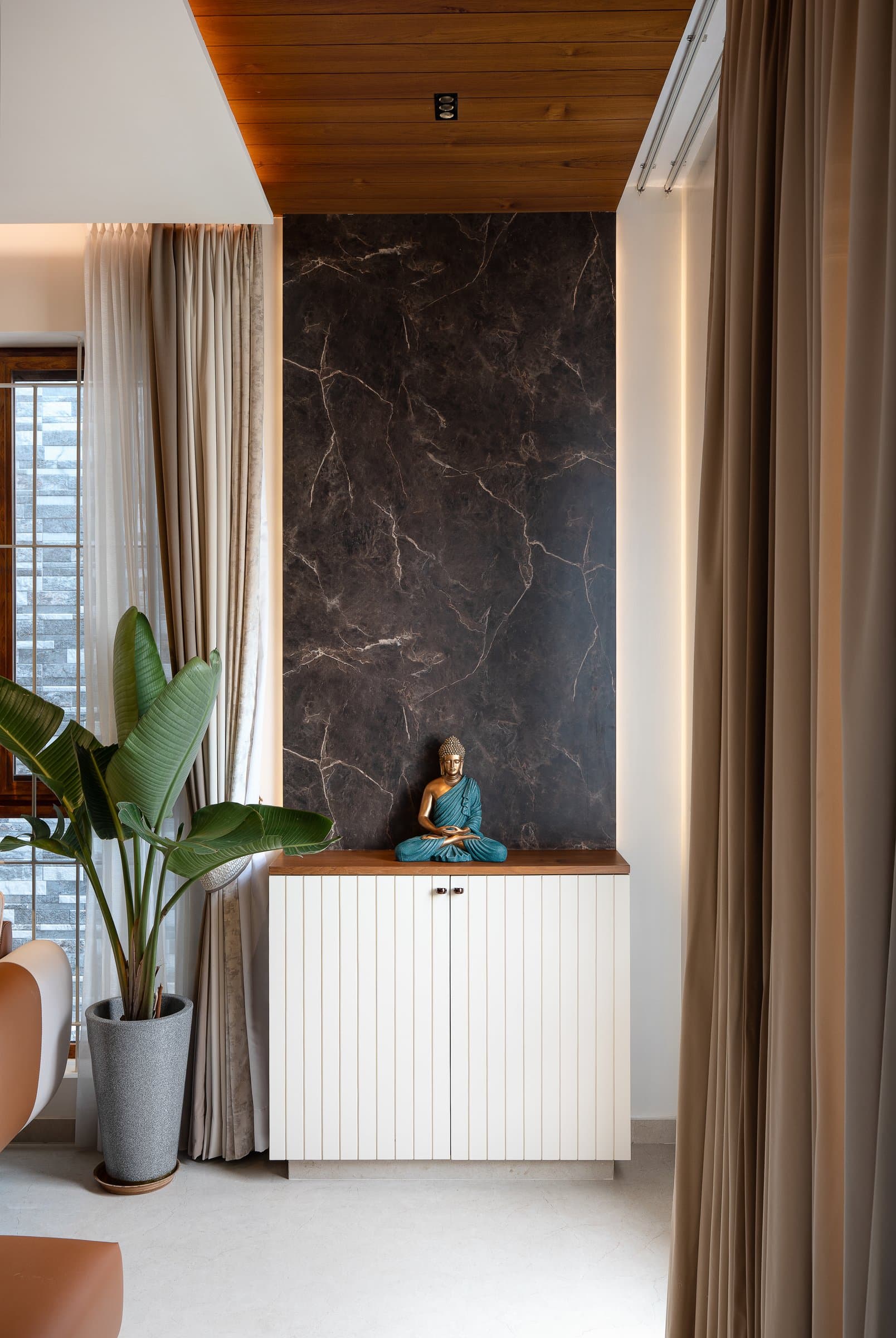 A niche between curtain runs: dark marbled stone, a fluted white console, and a single bronze figure