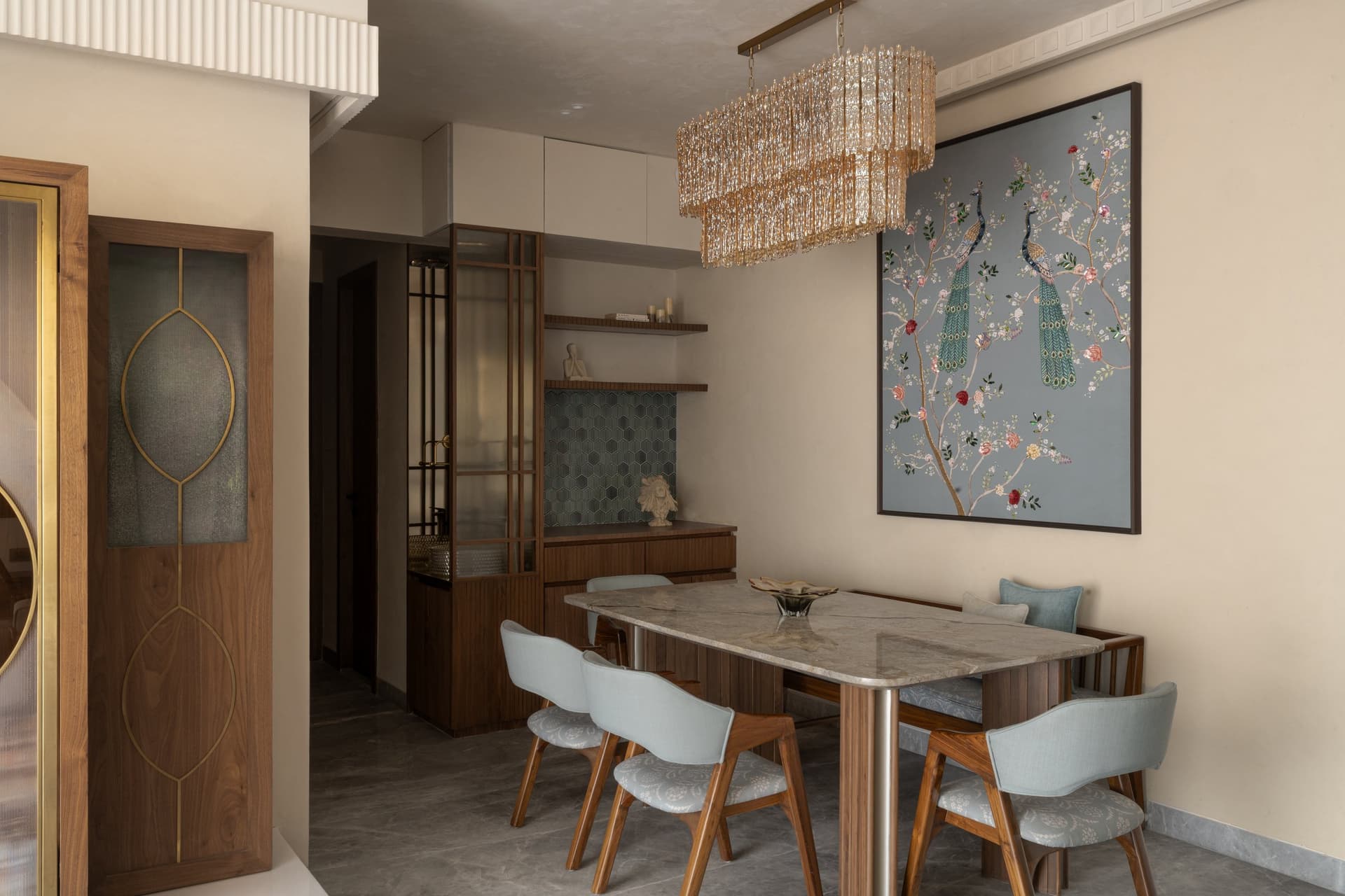 The dining zone gathers beneath a long crystal chandelier, the peacock artwork its emotional anchor