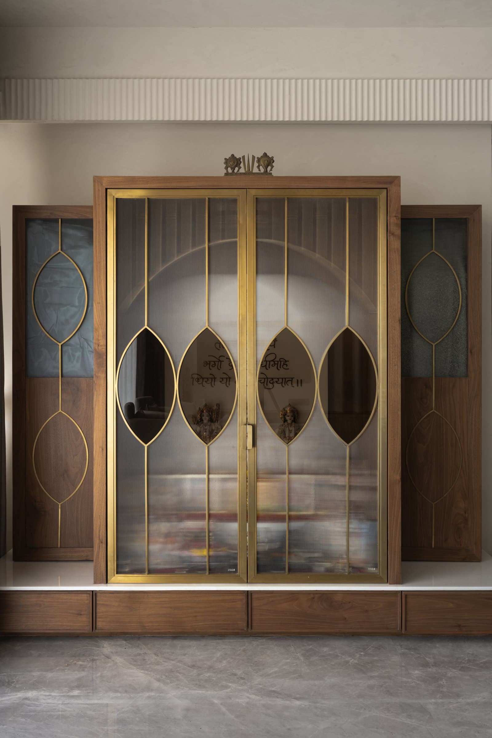 The mandir: a metal-and-glass casing holds a soft stone arch and the family's assembled deities