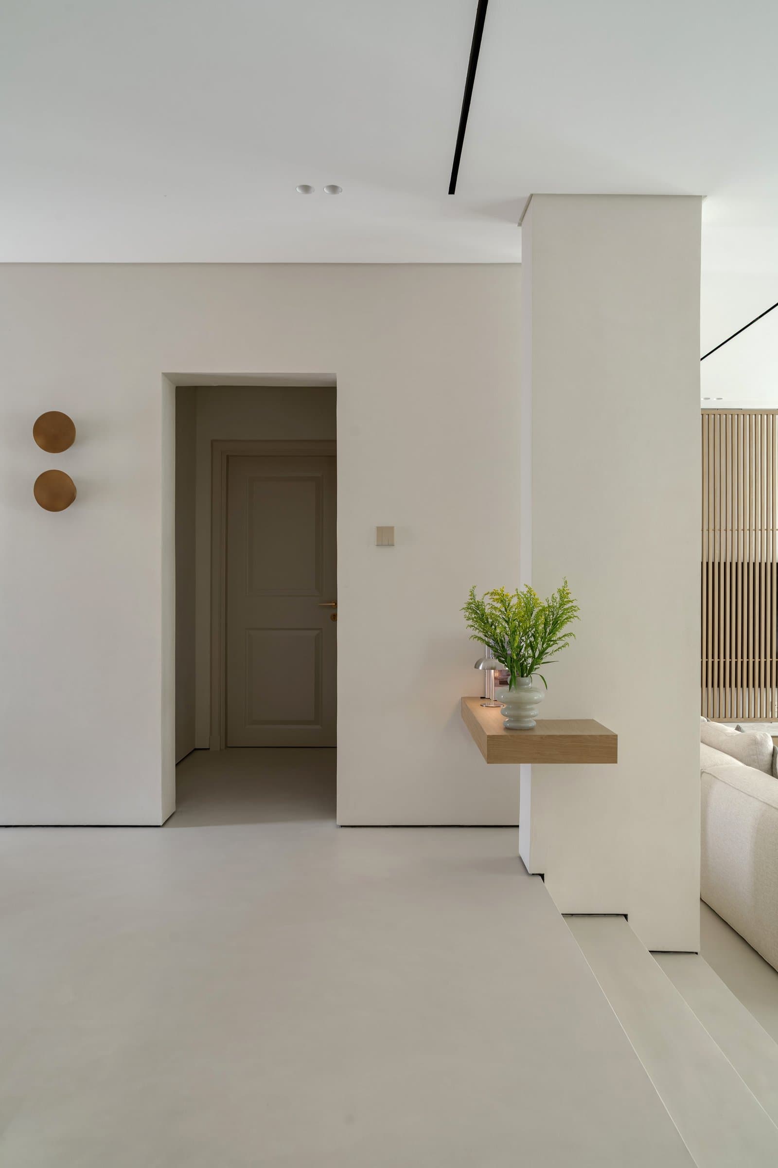 A threshold zone holds the restrained palette in plain view, with an oak ledge and brass wall discs setting the tone