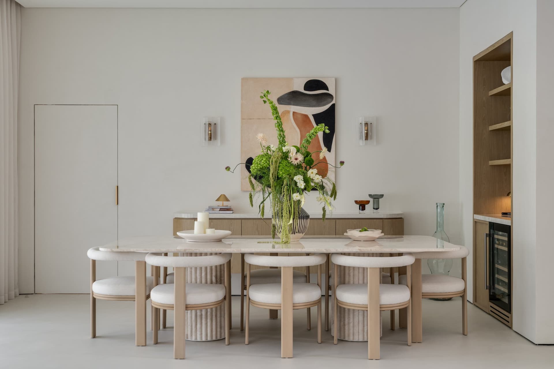 The dining room, centred on a custom travertine table surrounded by fluted oak chairs in ivory