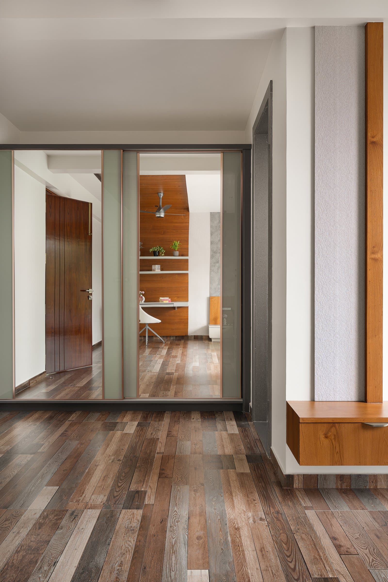 The vestibule to the private wing, organised by a slim wood-clad pier and a tall mirrored partition