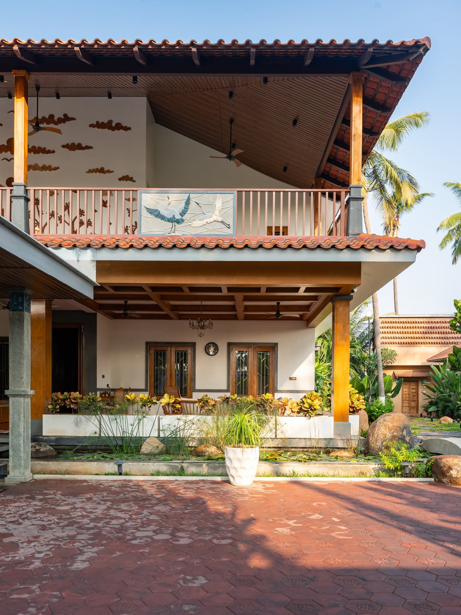 The rear elevation, where a lily pond and covered verandah anchor the ground floor beneath the cloud-mural balcony