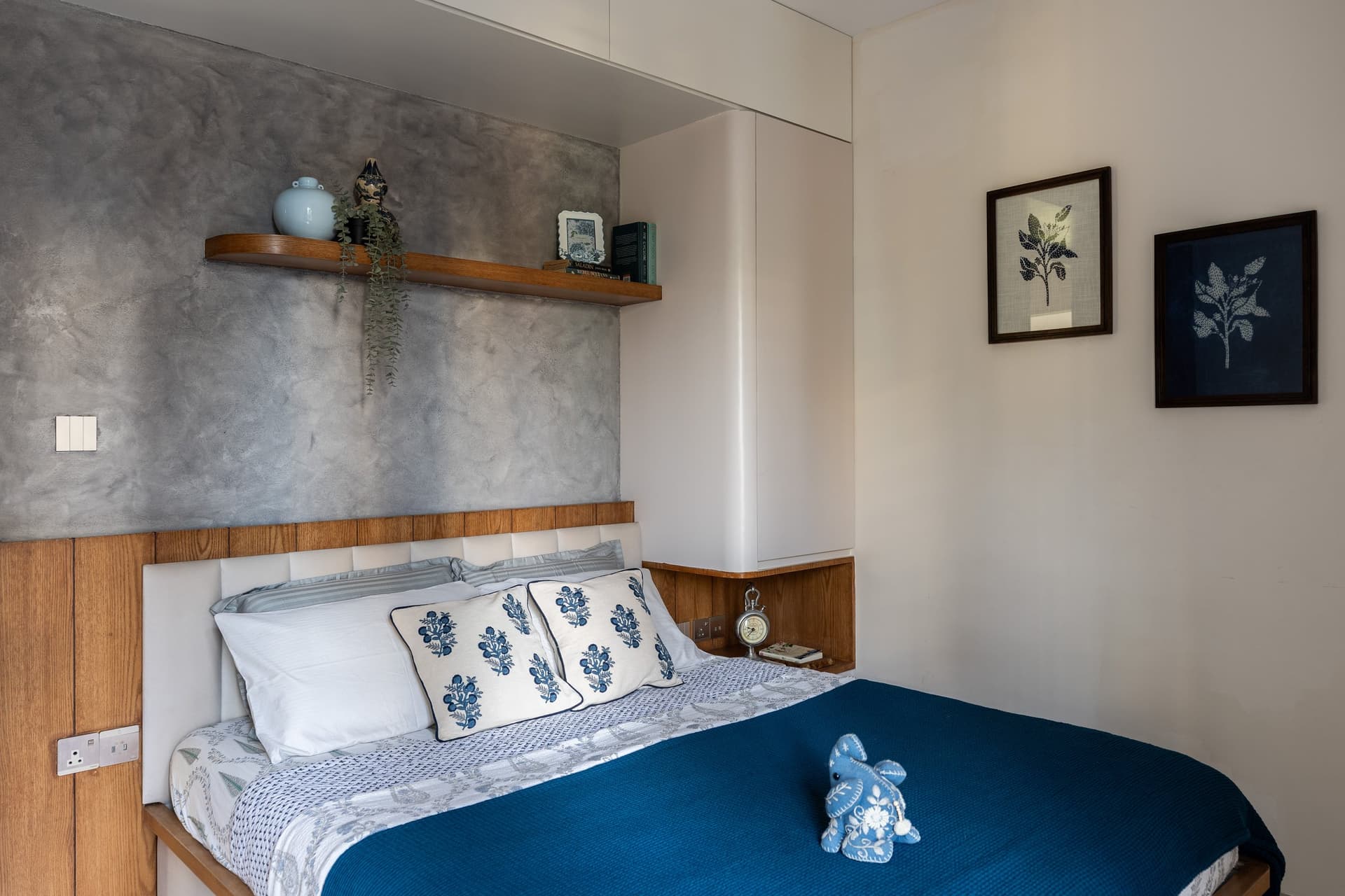 The second bedroom, warm oak framing a matte grey accent wall, with deep indigo linen introducing the room's decisive colour