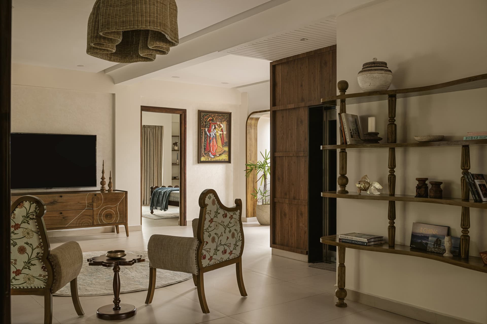 The first-floor informal living, where woven pendant, turned-post shelving, and crewel-upholstered armchairs frame the passage to the bedroom wing