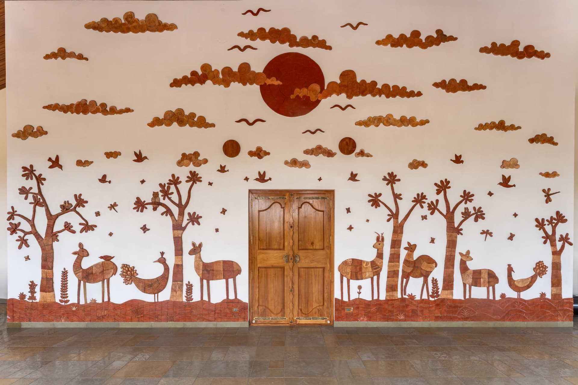 The double-height entry wall, where a hand-carved clay forest scene from northern India spans the full elevation
