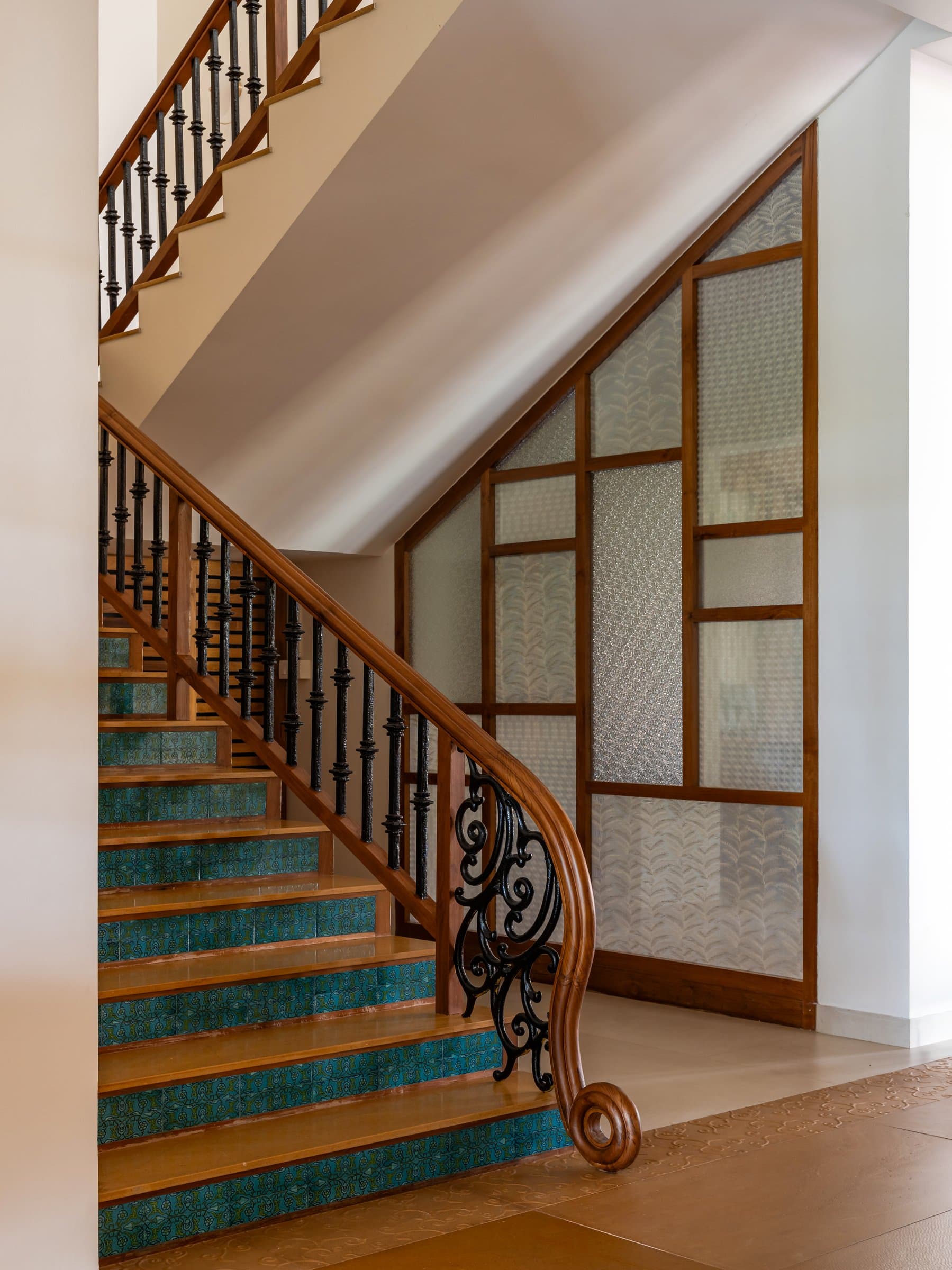 The staircase, where teal encaustic tile risers meet a scrollwork iron balustrade and reeded glass screen