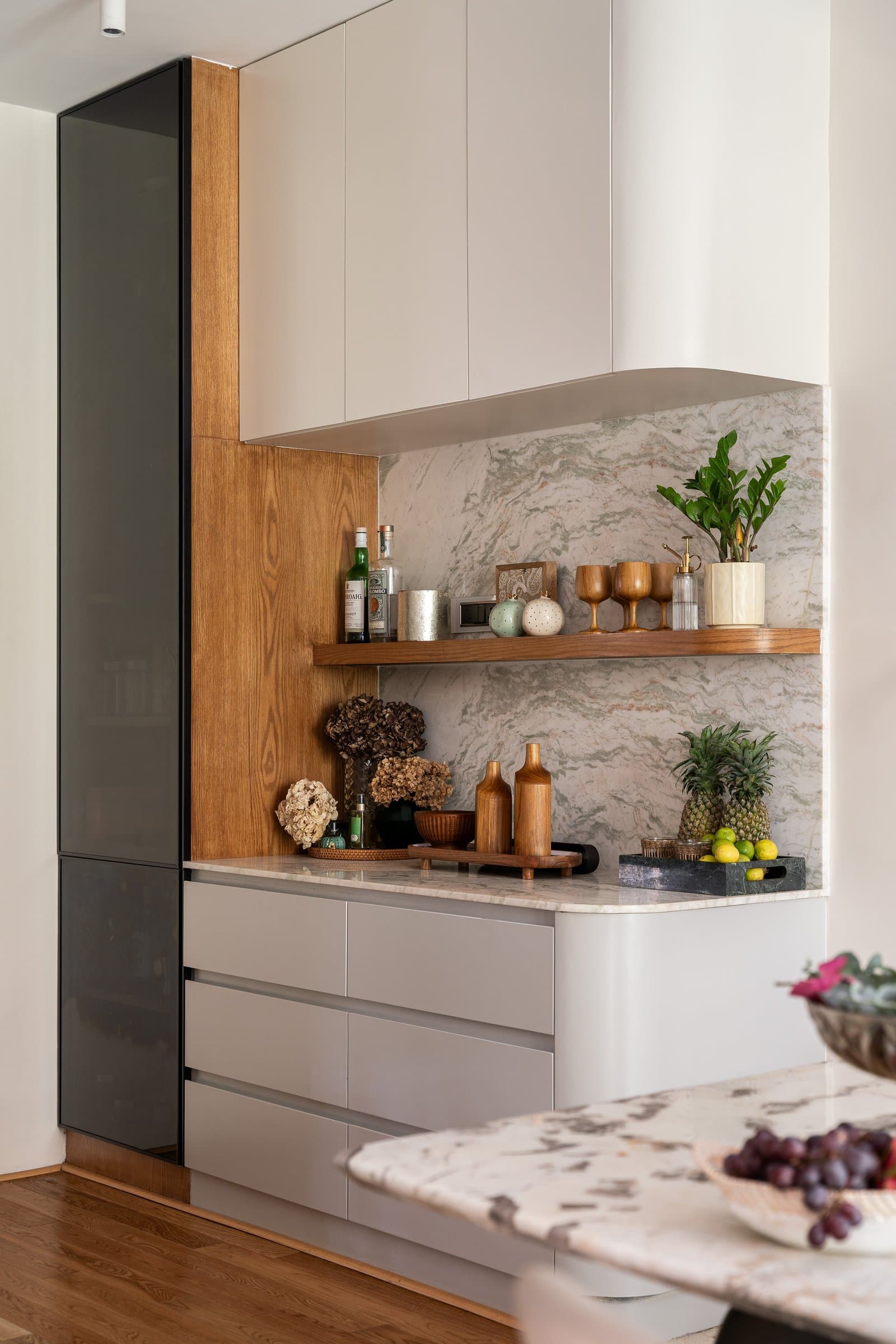 The bar zone, warm oak and veined stone meeting soft-close cabinetry in warm greige
