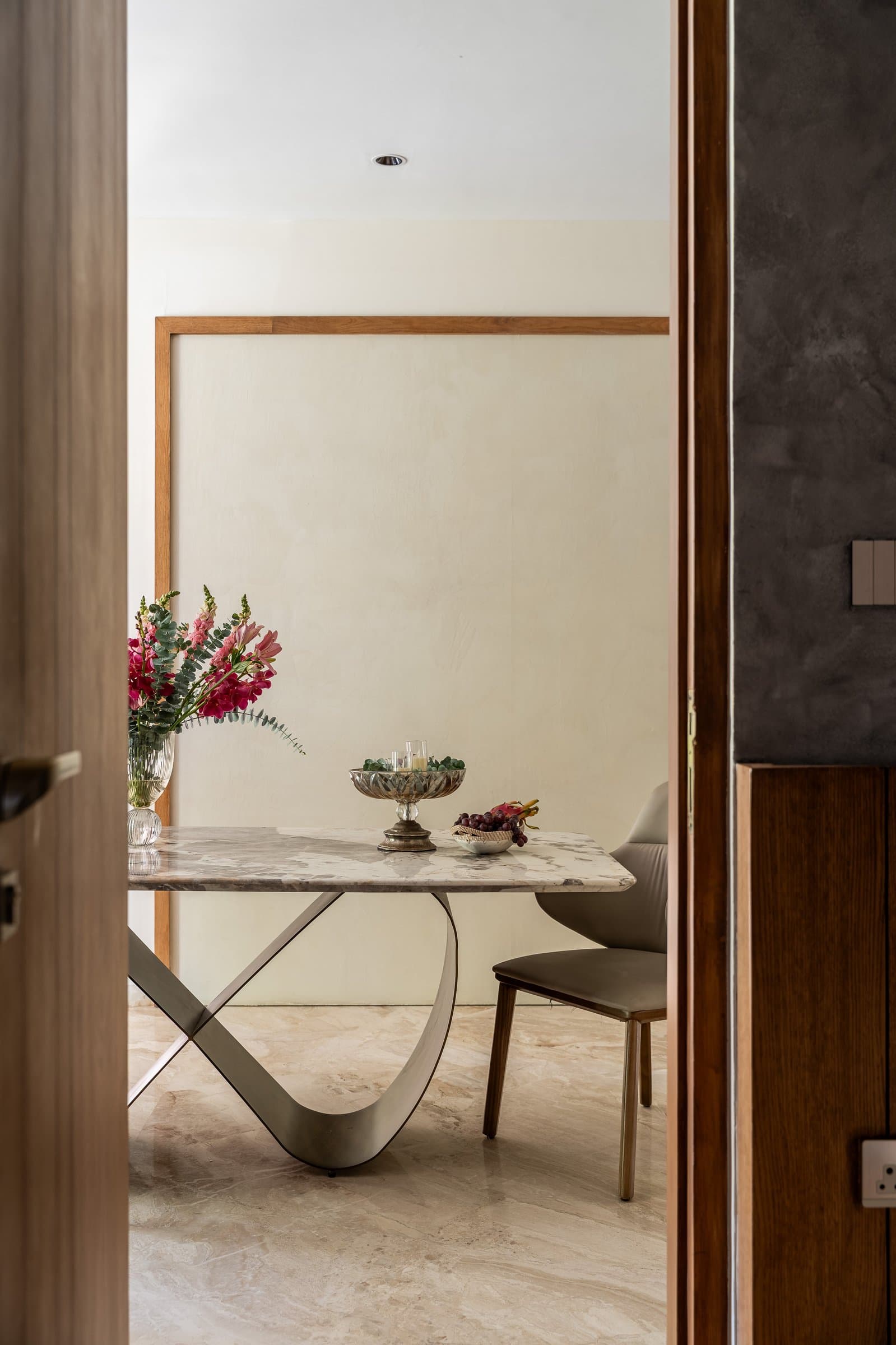 The dining table's looped steel base against a limewashed cream wall framed in warm oak