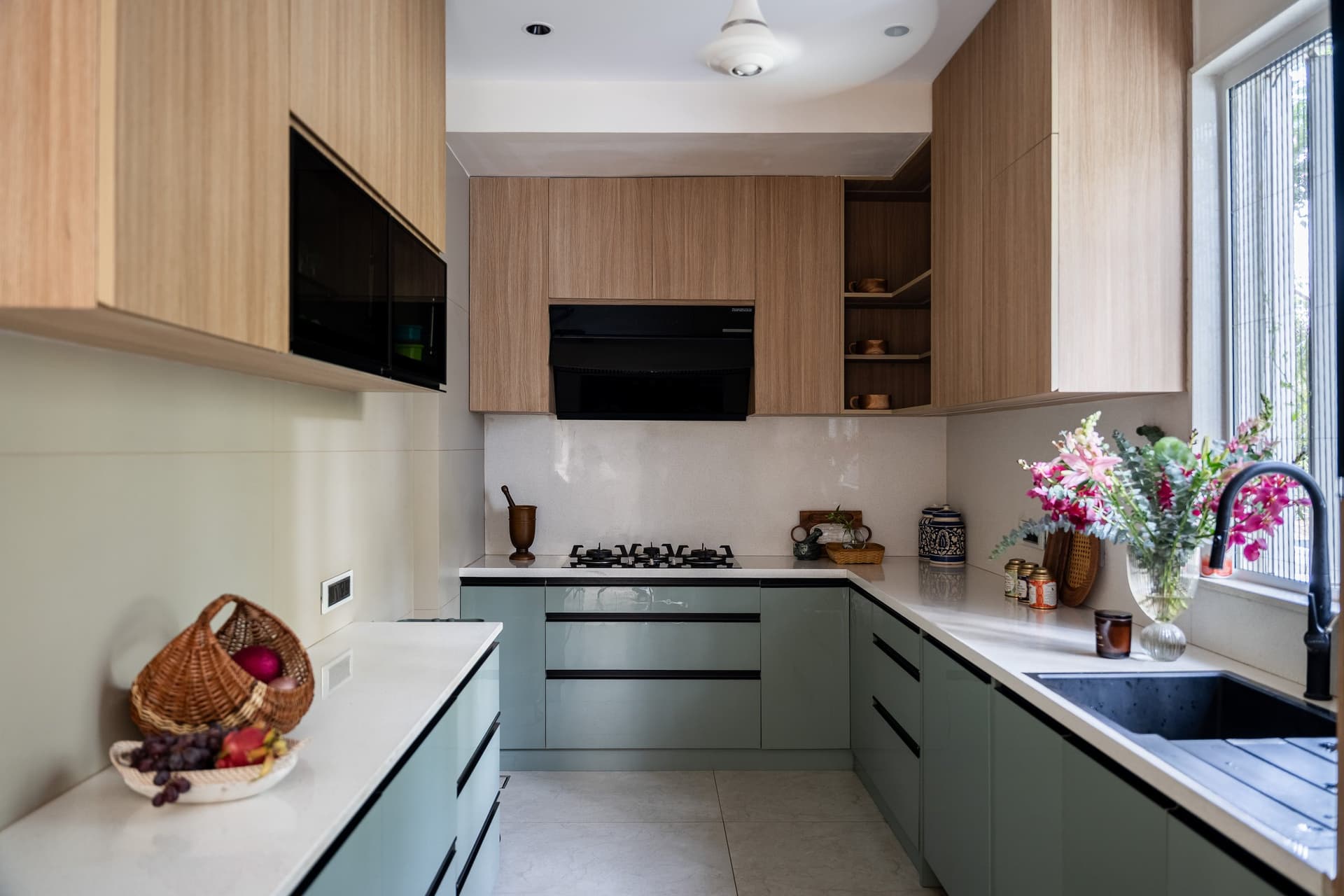 The kitchen, sage-green base cabinets and warm oak uppers framing a window onto the neighbourhood's greenery
