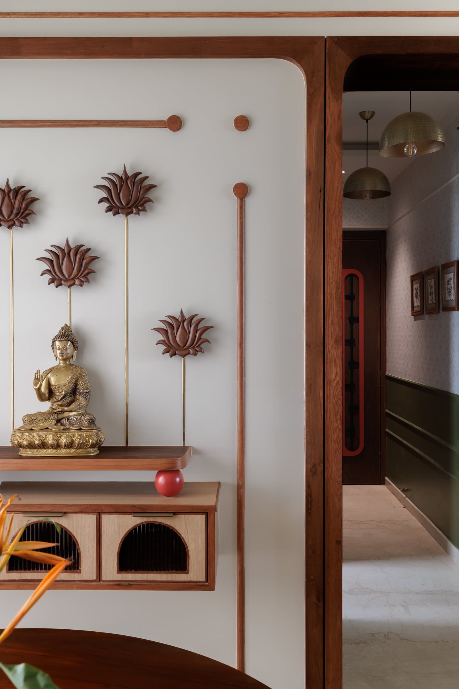 The puja alcove, where carved lotus stems and a brass Buddha compose a structured tableau above arched-front drawers