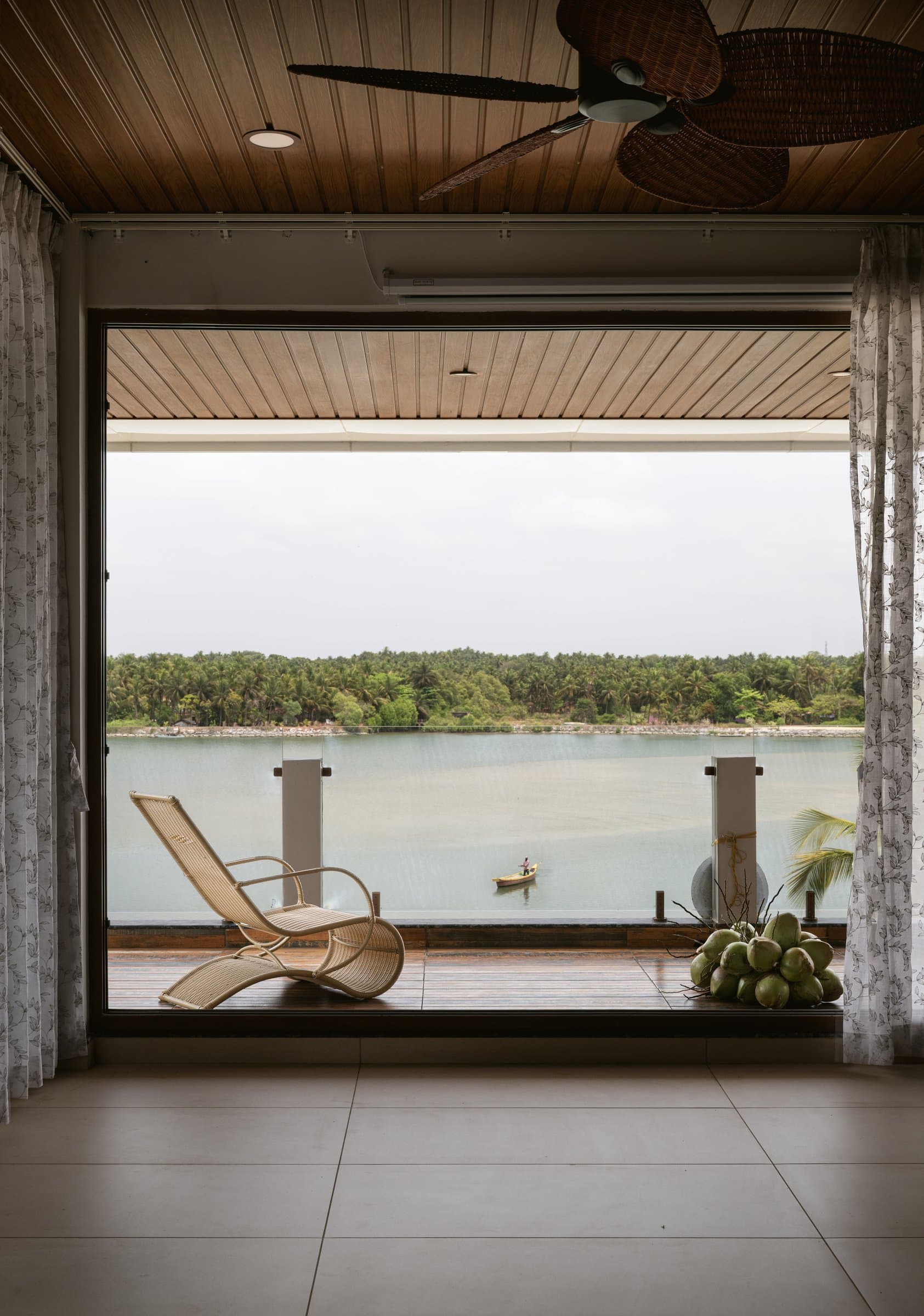 The gathering pavilion, where a cane lounger and tender coconuts face the river through a wide opening