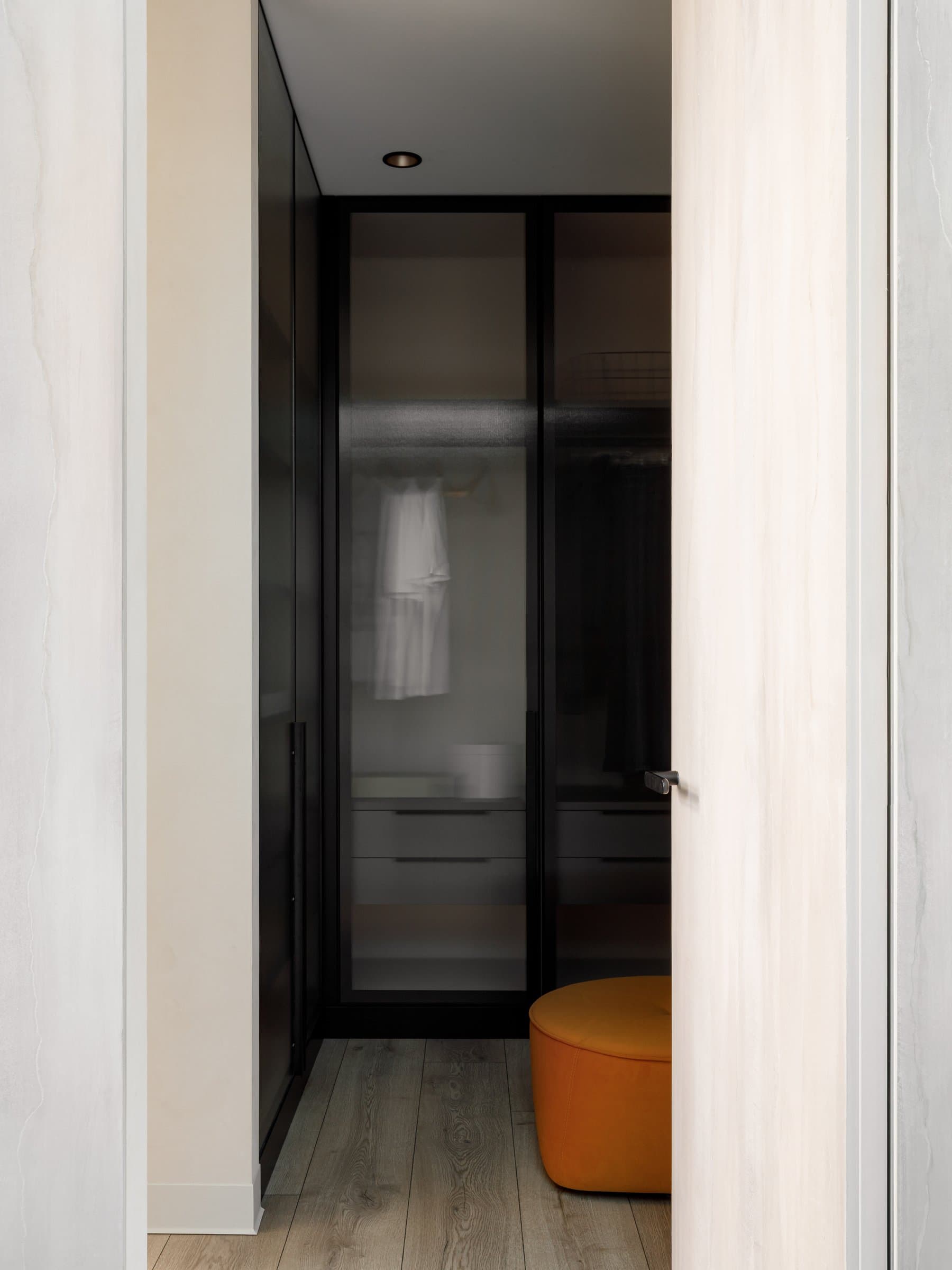 The dressing corridor, where tinted glass wardrobes sit against a travertine door casing
