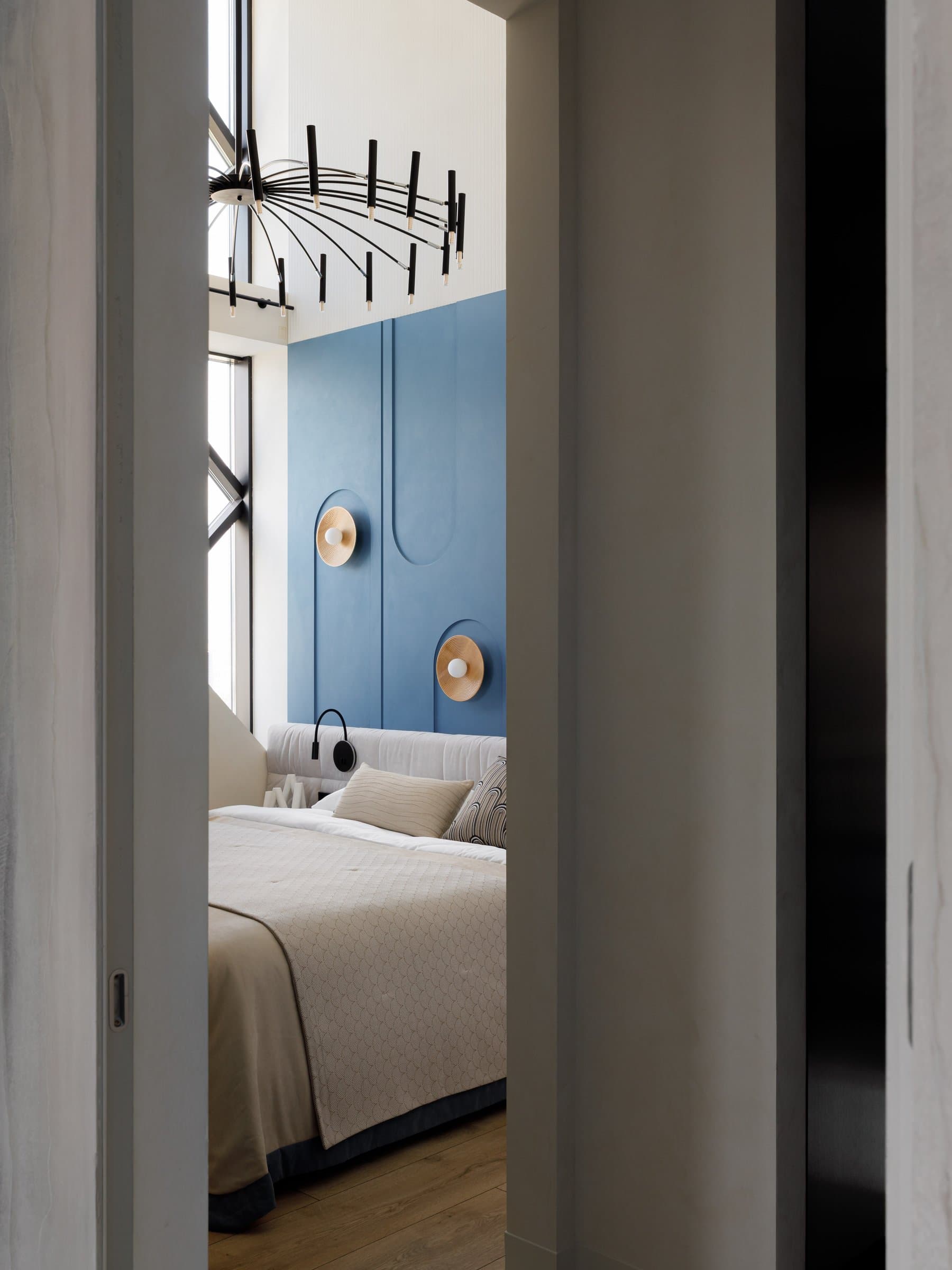 The double-height volume above the bed, punctuated by rattan wall lights and a linear chandelier