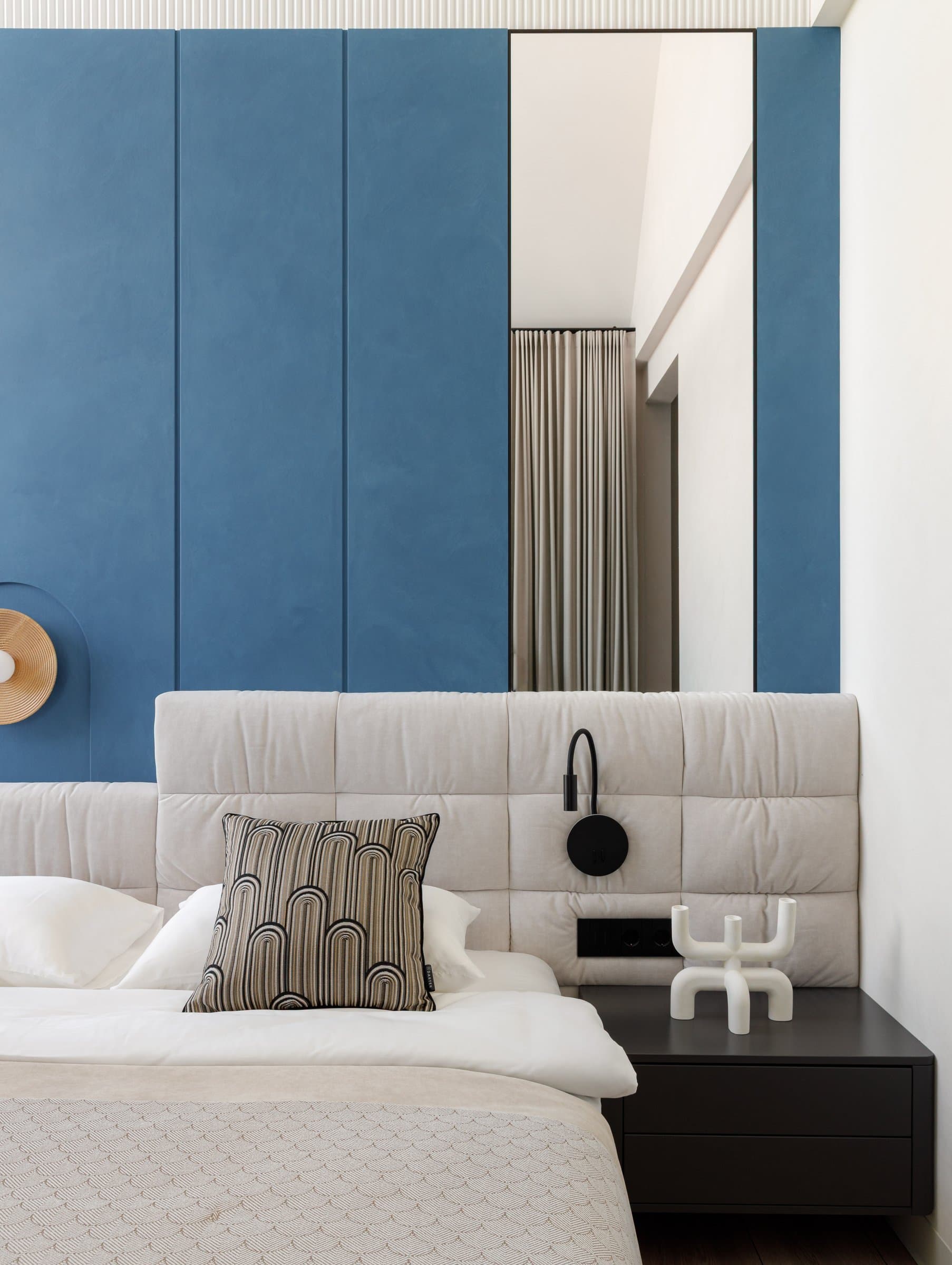 The primary bedroom, where blue panelling frames a linen-upholstered headboard