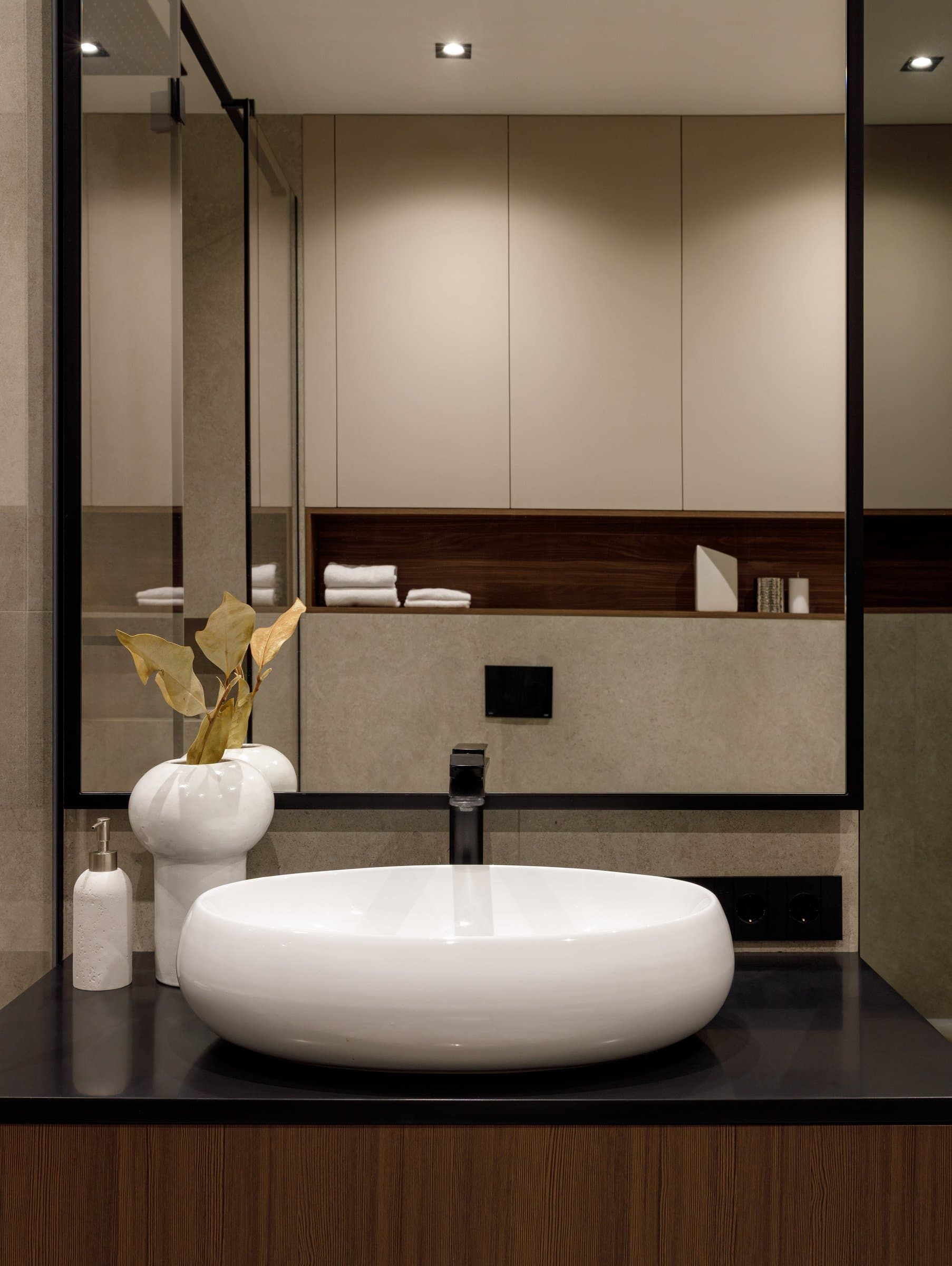 The powder room, where warm walnut and dark stone frame a rounded ceramic vessel