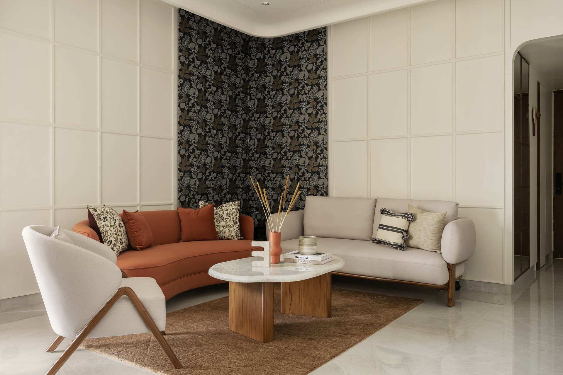 The living room, where a panel of botanical wallpaper set within moulded framing anchors a terracotta curved sofa