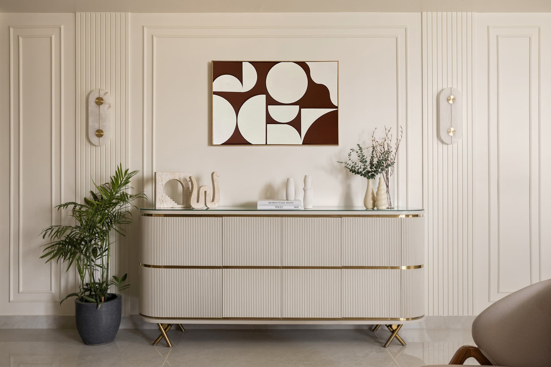 The entry console vignette: reeded panelling and travertine objects beneath an oxblood and cream artwork, flanked by paired alabaster sconces