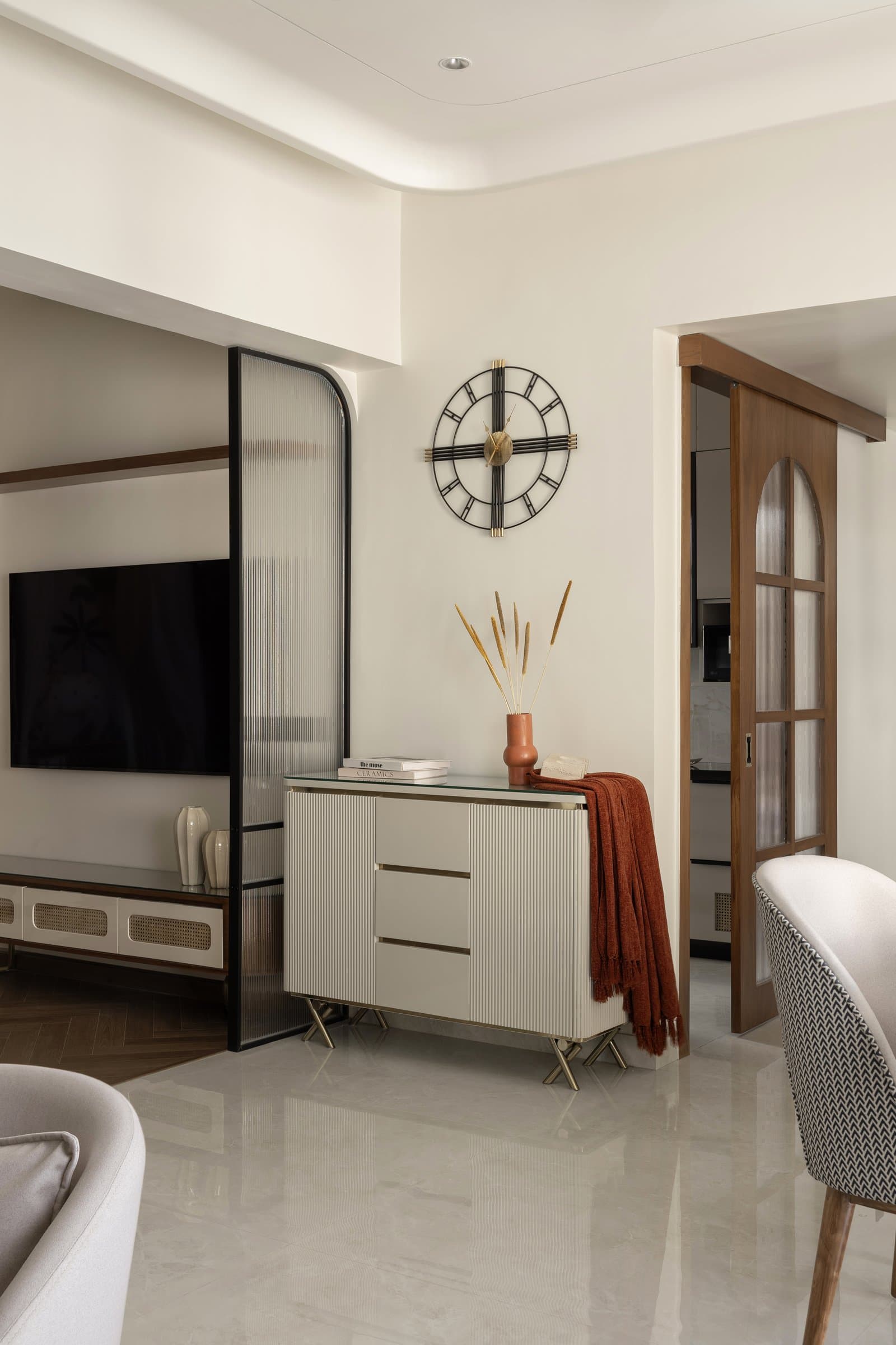 The media wall, where a fluted console and reeded glass screen filter sightlines toward the kitchen beyond