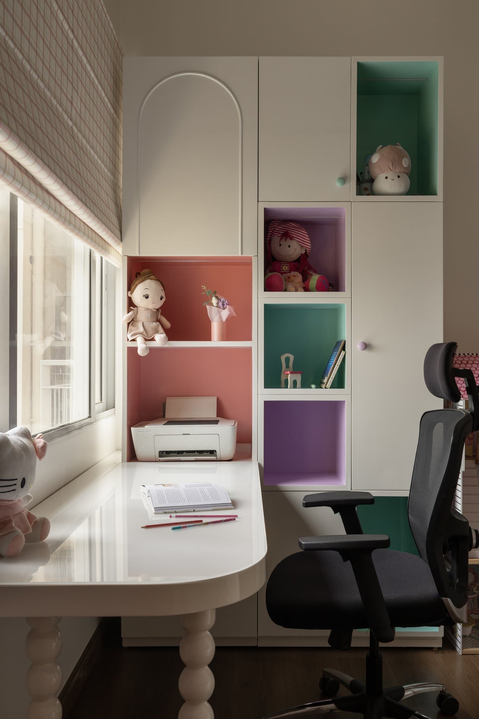 The study nook within the daughter's room, where coral, mauve, and green cubbies turn storage into composition