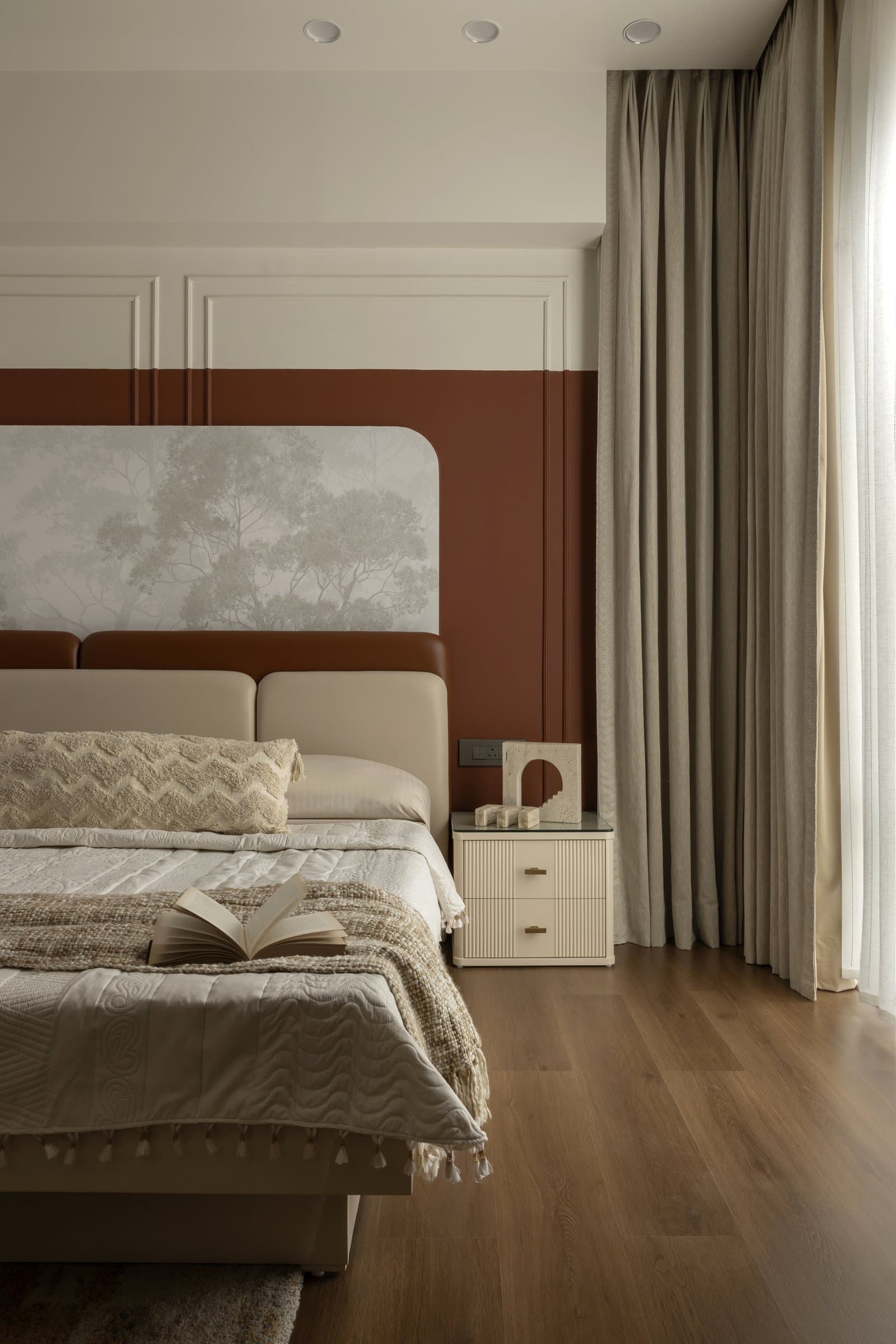 A closer view of the master bed, where layered textiles sit against warm wood flooring and pooled linen curtains
