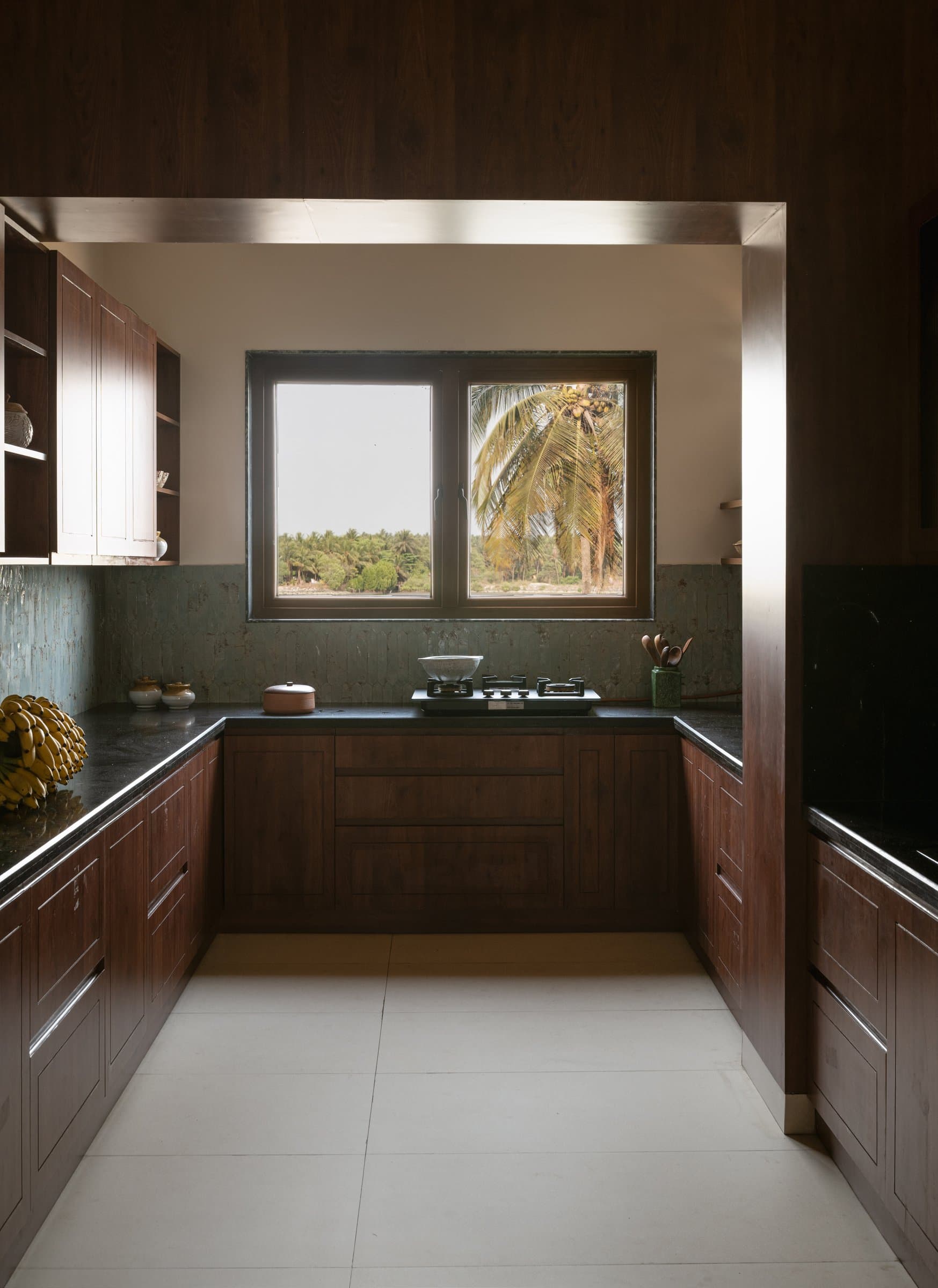The kitchen, where dark wood cabinetry and a sage backsplash frame a window onto the coconut grove