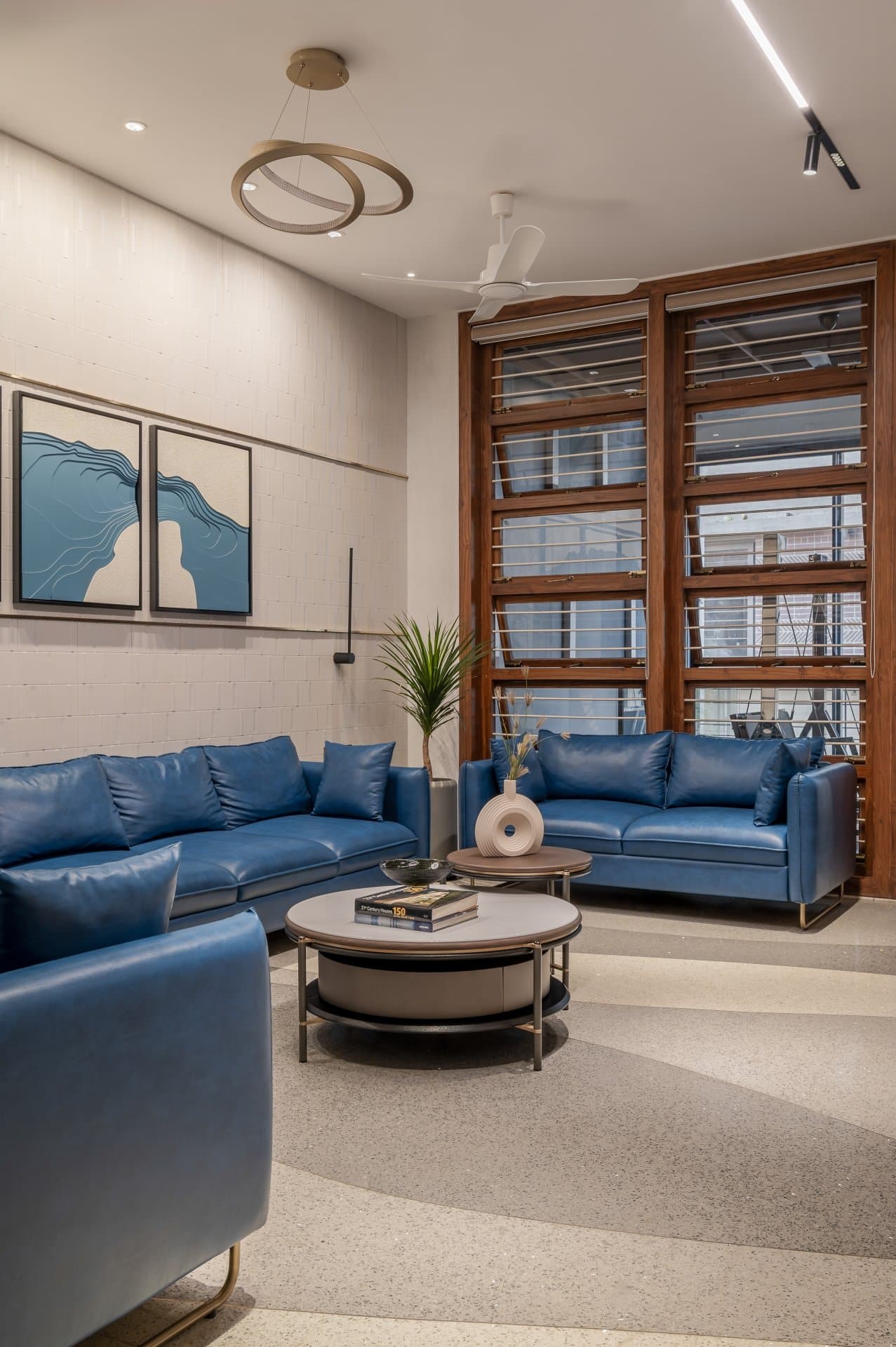 The formal living room, where deep blue leather sofas and tall timber-framed windows hold the double-height volume