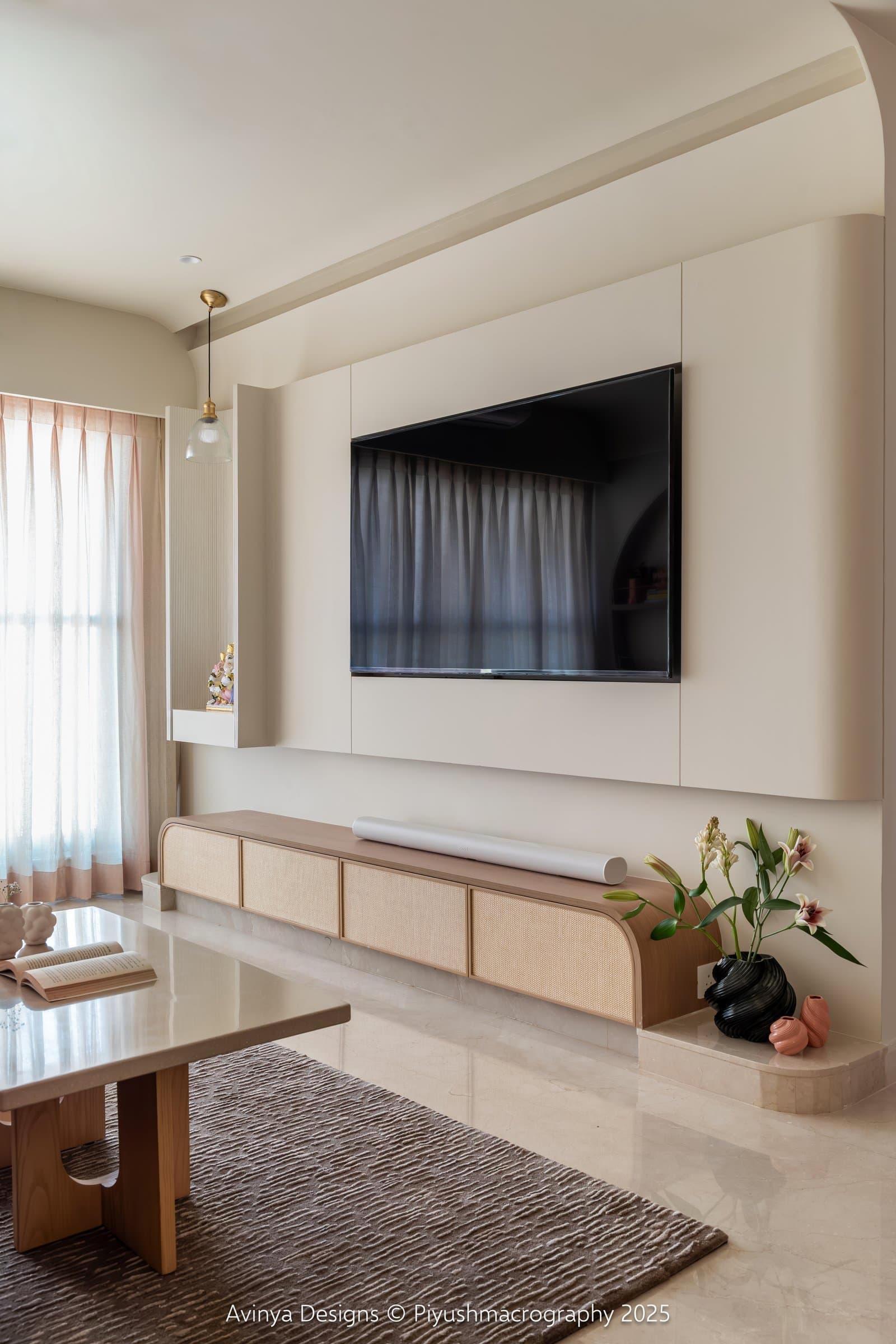 The media wall, where a cane-fronted console sits on a stepped stone plinth beside a reeded pooja niche