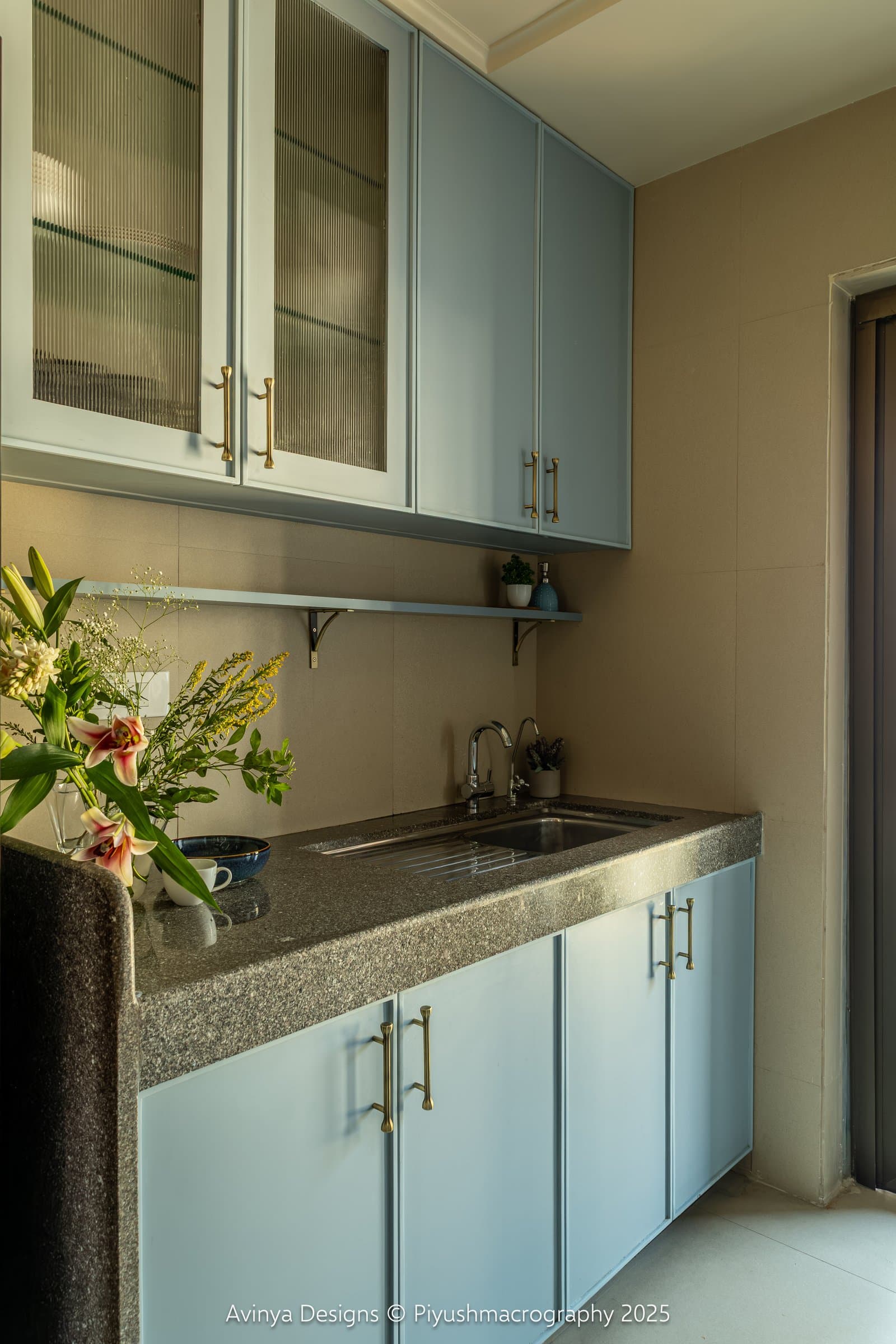 The utility counter, where reeded glass fronts and a floating shelf resolve the sink zone against a warm taupe tile wall