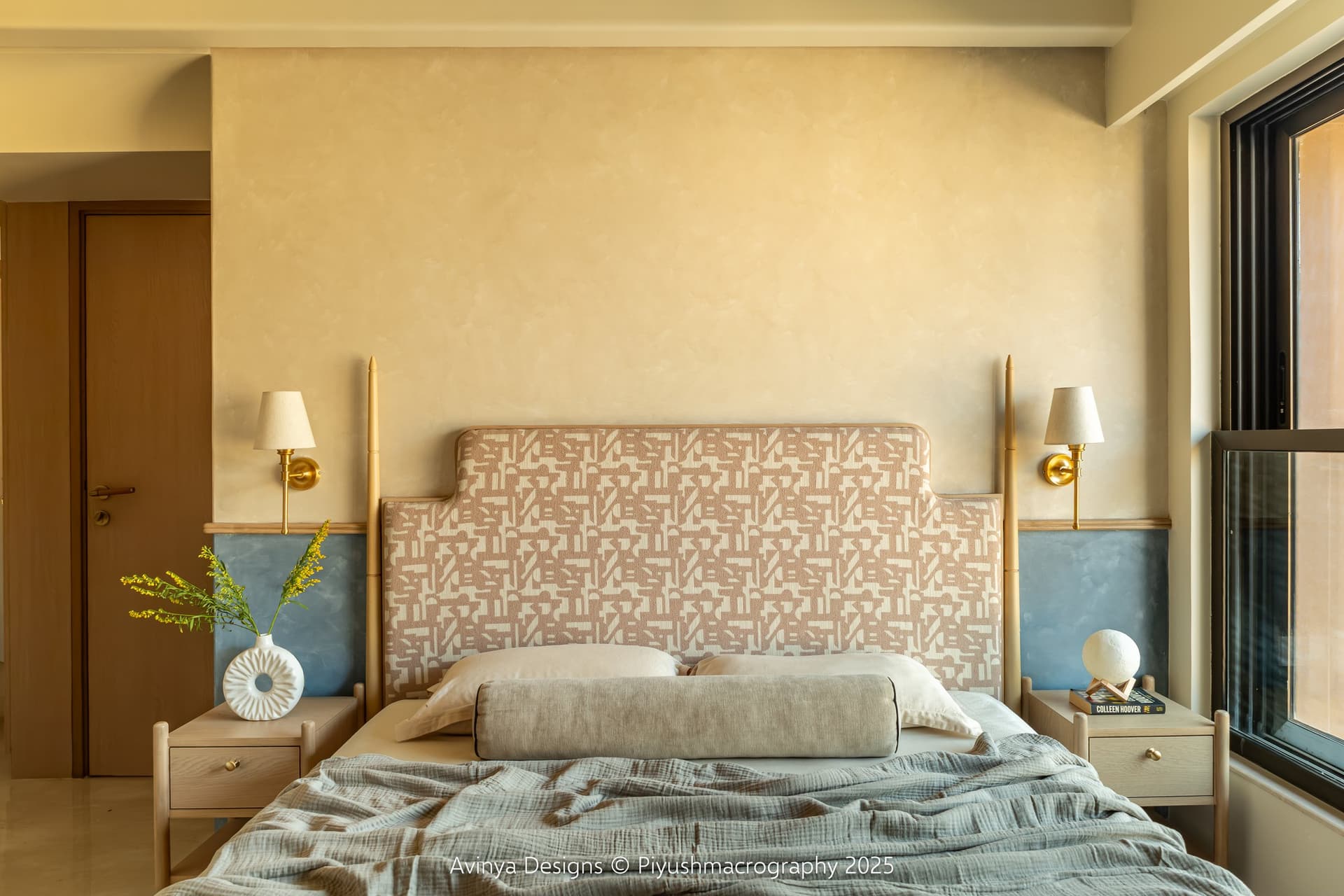 The master bedroom, where a limewashed ochre wall meets a dusty blue plaster dado behind the upholstered headboard