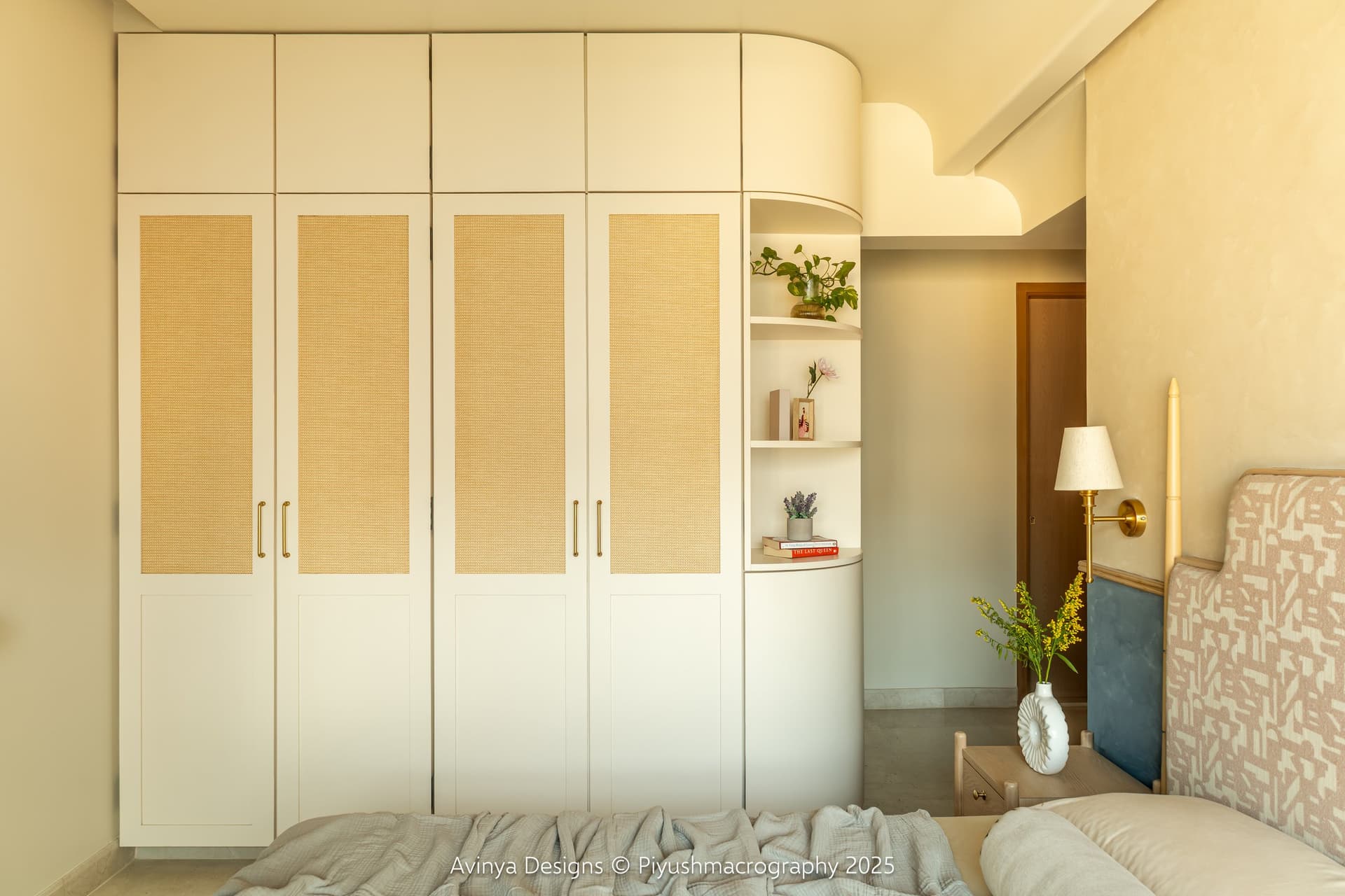 The master bedroom wardrobe wall, its cane-webbed cabinets meeting a rounded corner column of open shelves