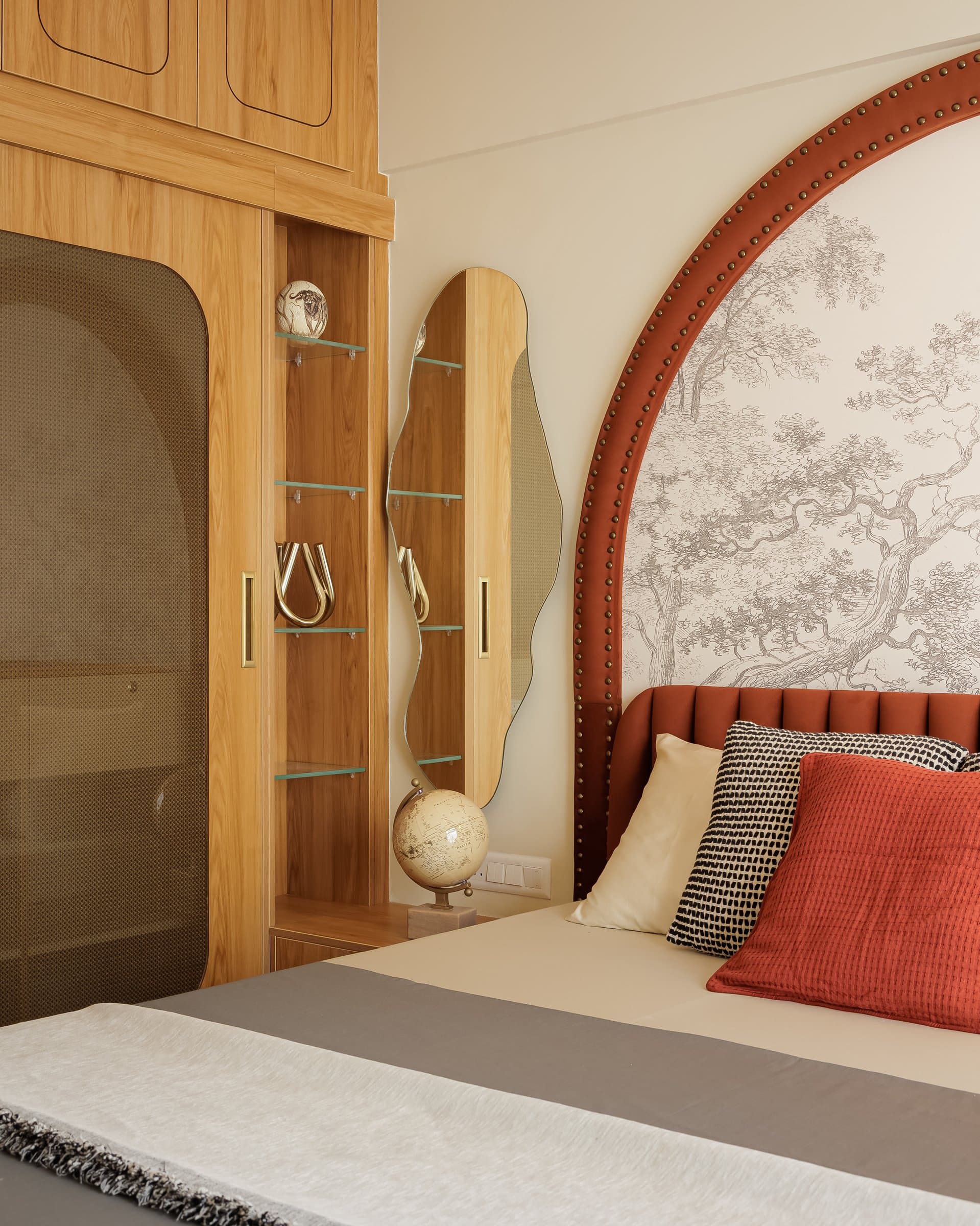 Opposite the master bed, a cane-inset wardrobe and slender display column with a wavy-edged mirror