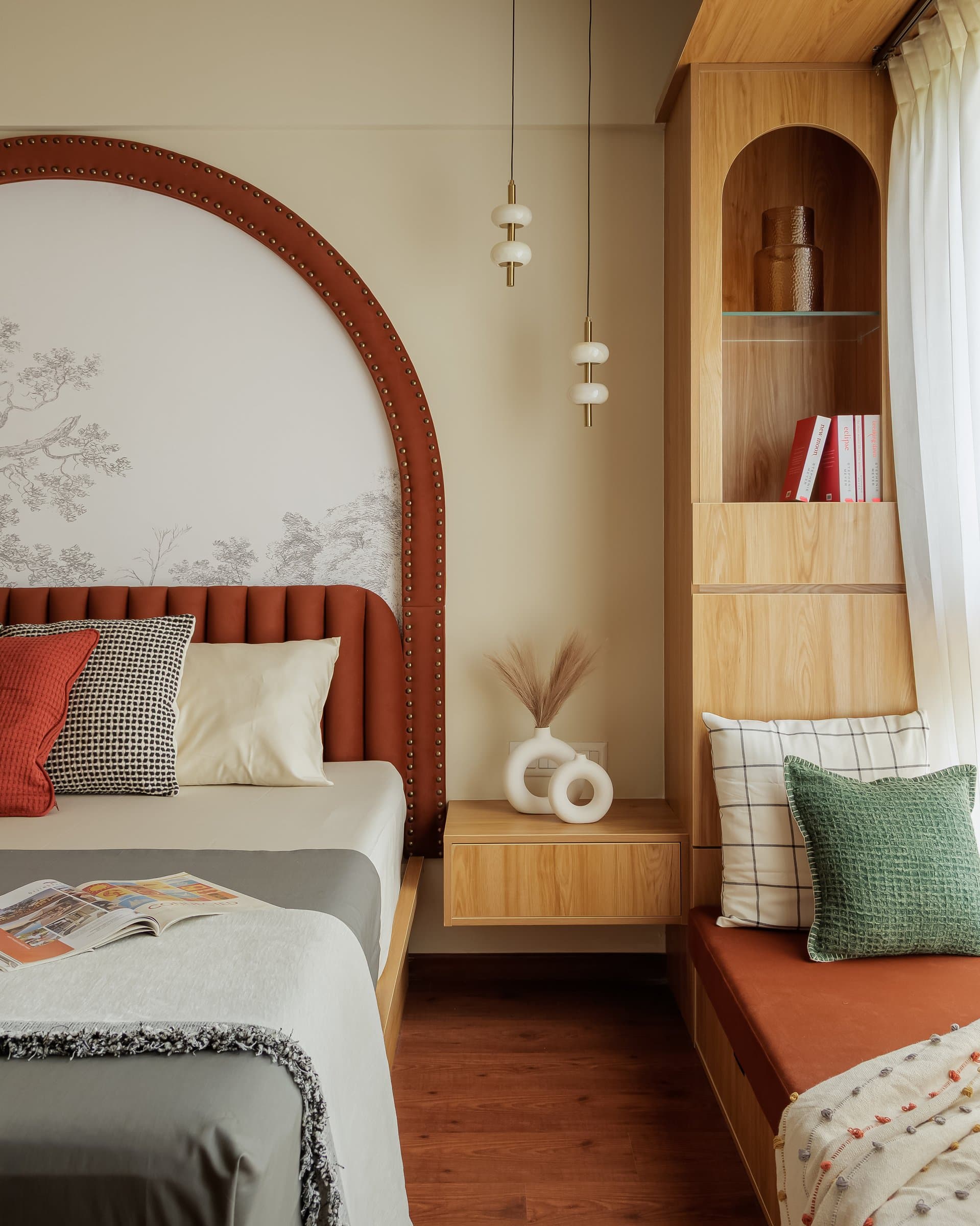 A closer view of the bedside, where twin pendant lights descend beside an arched niche folded into the joinery