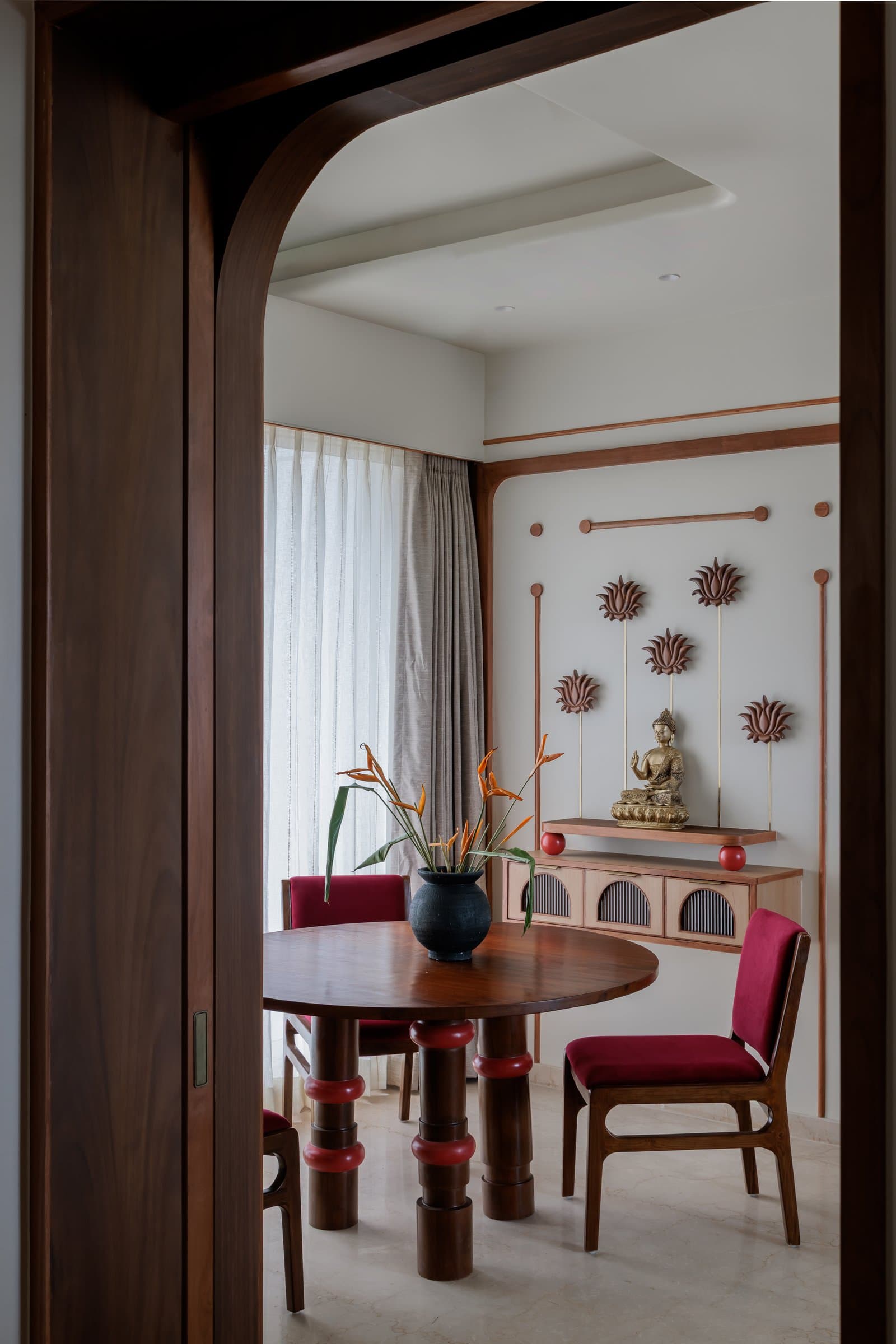 The dining zone, framed by a teak archway with the puja alcove composed behind