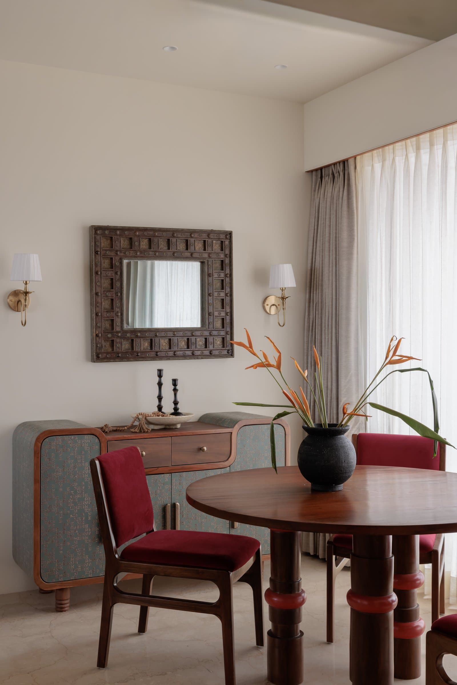The dining sideboard, where a heavily studded antique mirror sits between twin brass sconces above muted teal cabinet panels