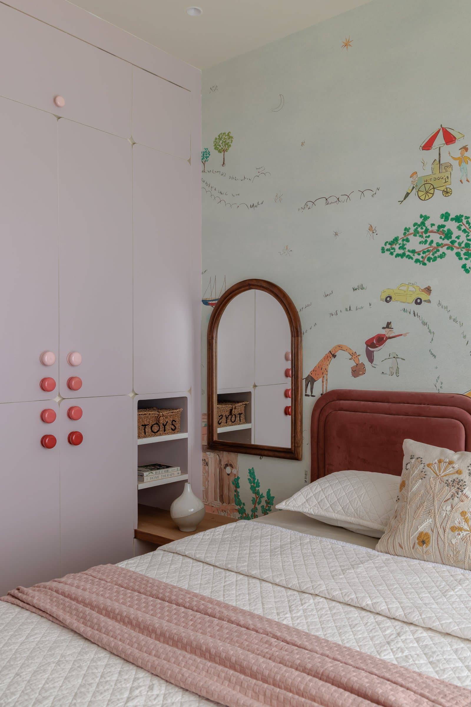 The child's wardrobe, its soft-pink doors punctuated with a graded cluster of red and pink medallion knobs