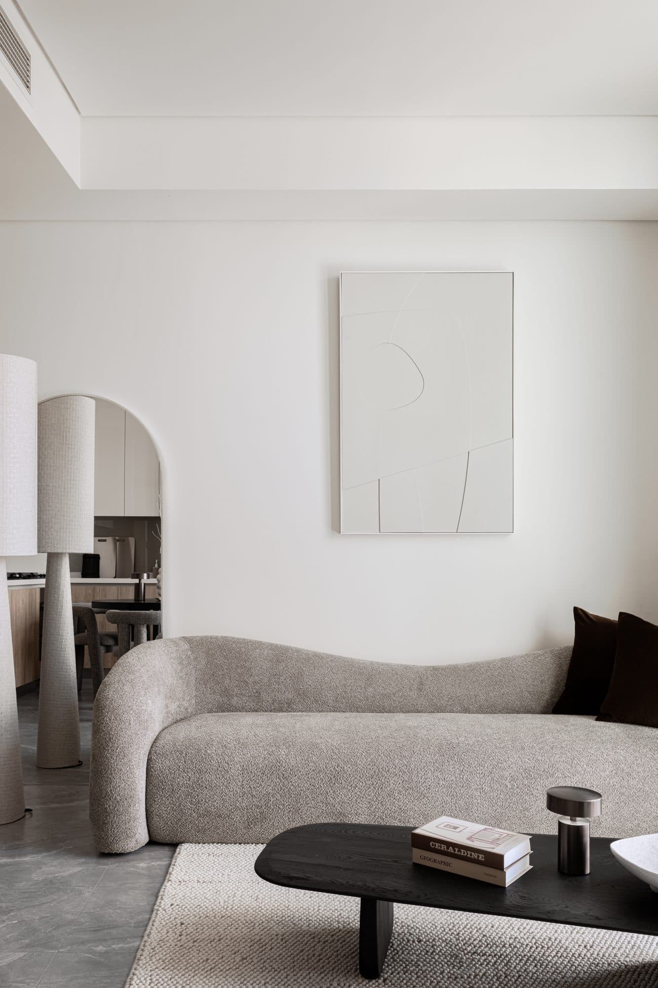 A boucle-curved sofa against a pared abstract painting — a single architectural gesture set inside a limited-budget shell.