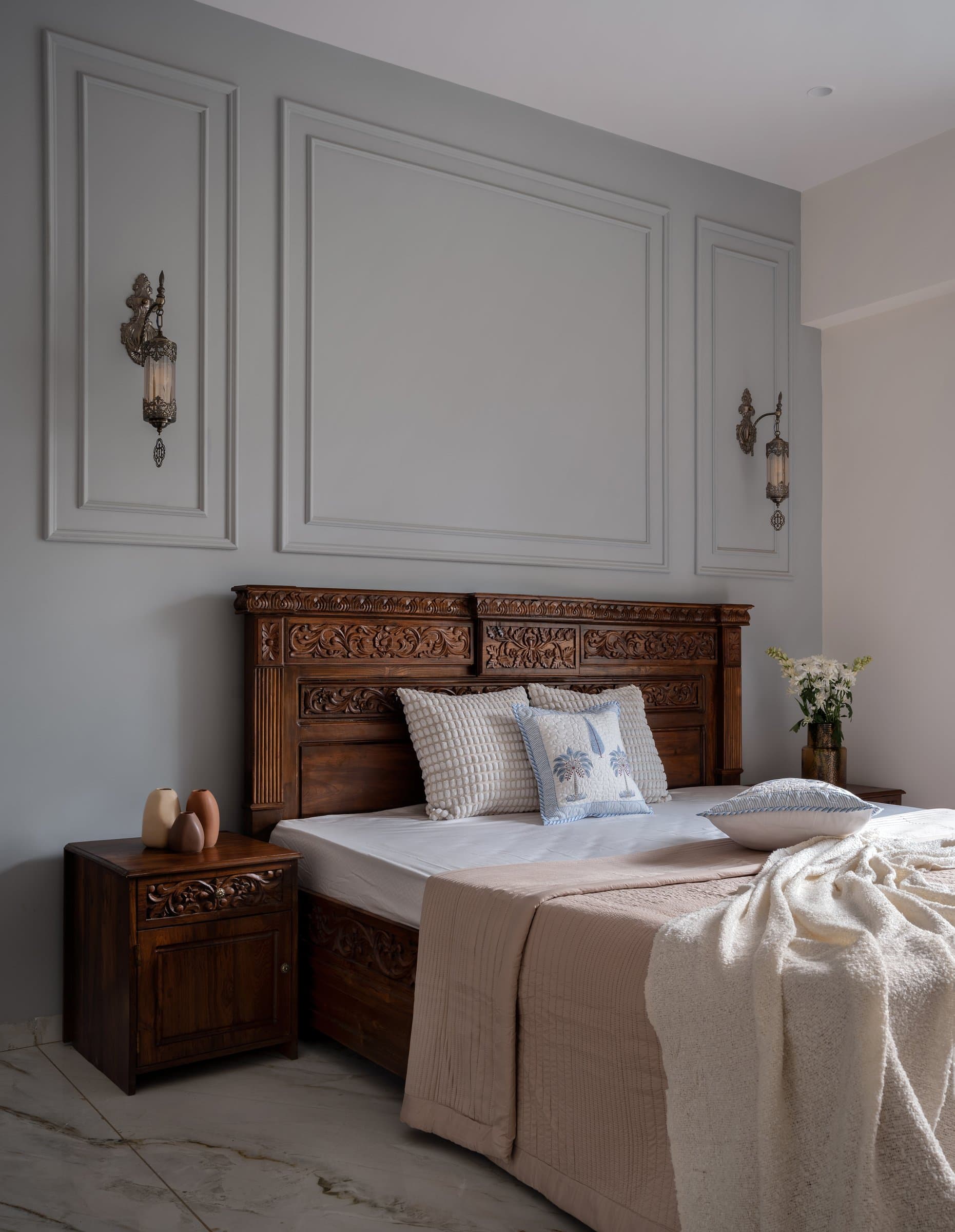 The guest bedroom, where a pale grey wall articulated with classical panel moulding frames another carved teak bed