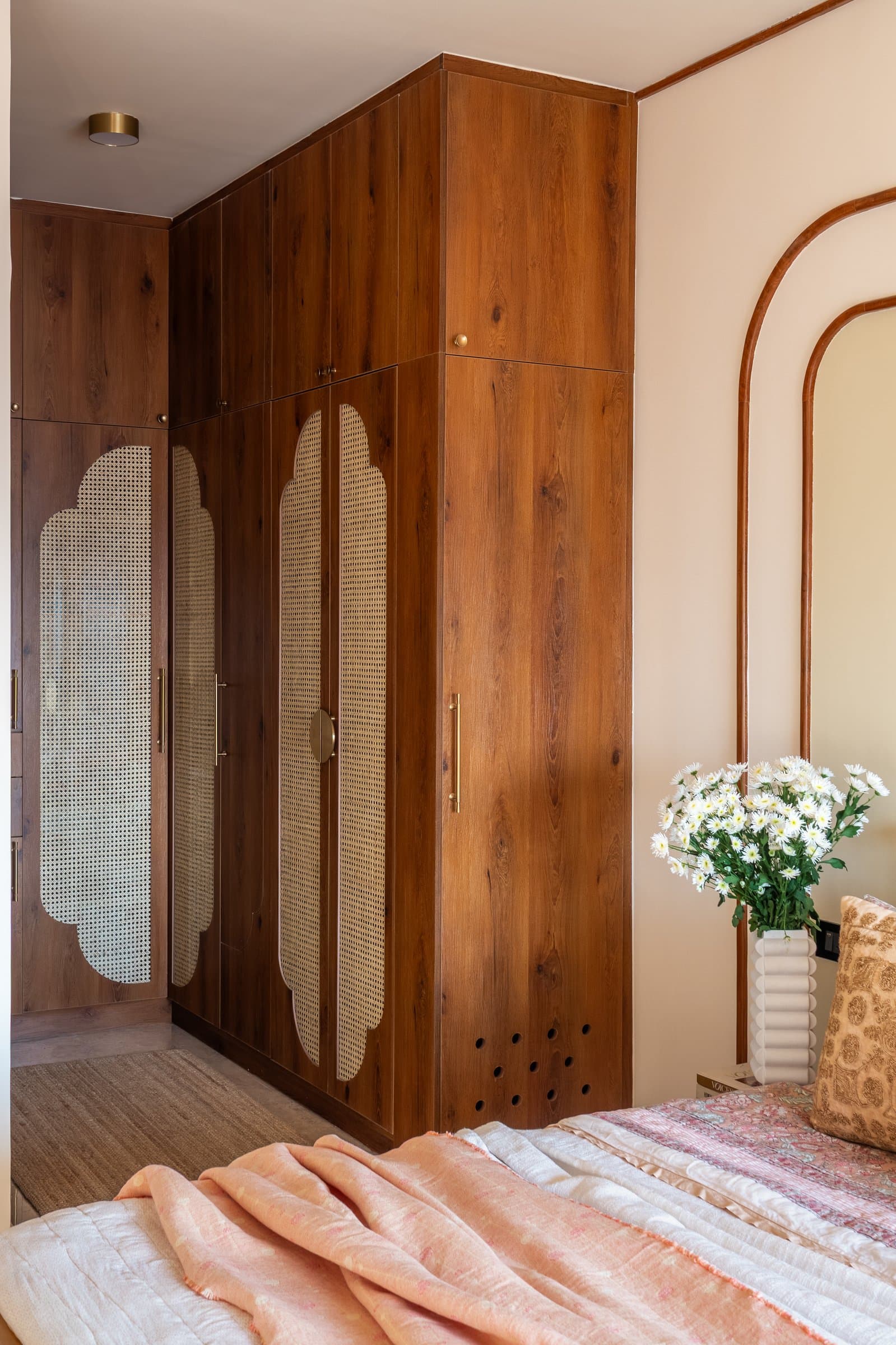 The master bedroom wardrobe, where scalloped cane-woven panels set into warm-toned doors read as architecture rather than joinery