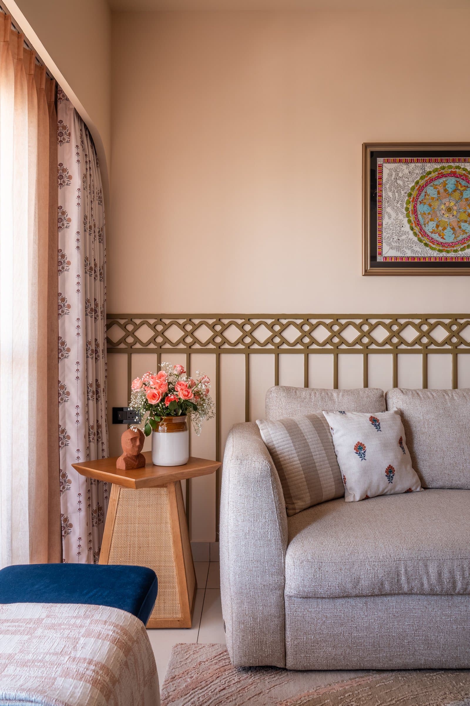 A second corner of the living room, where a decorative metal grille and a block-printed curtain frame the arched opening to the pooja area