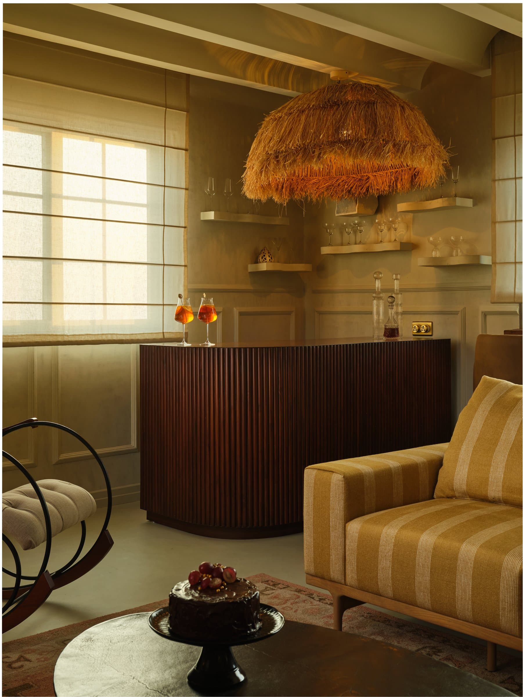 The bar, where a curved fluted counter meets a shaggy raffia pendant in a corner of gilded light