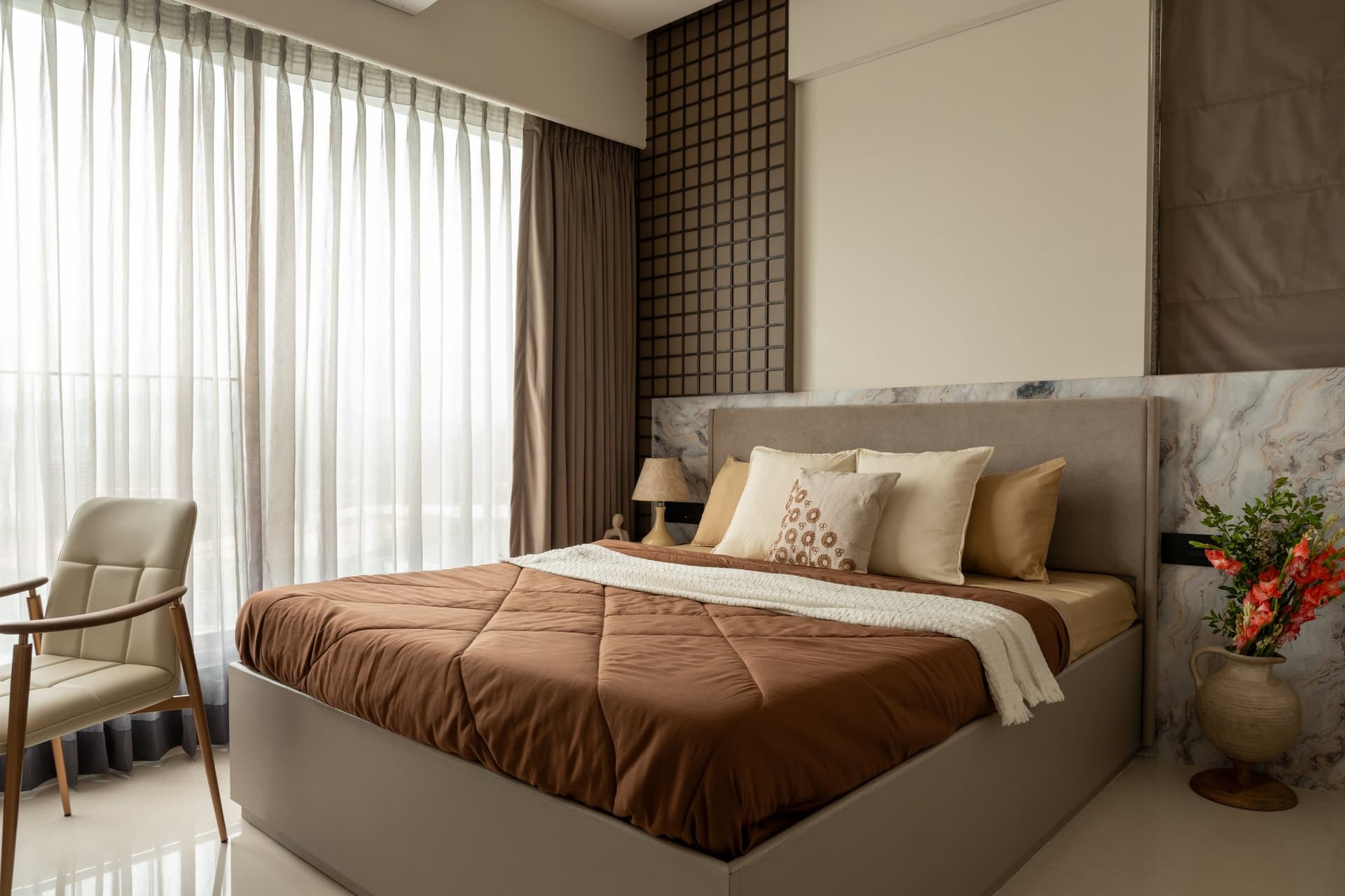 The master bedroom, where a wide upholstered headboard sits against a band of veined stone and a dark grid panel