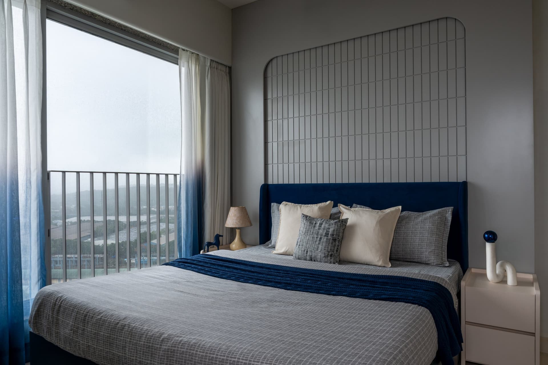 The third bedroom, where a deep blue headboard sits beneath a tall wire-grid panel