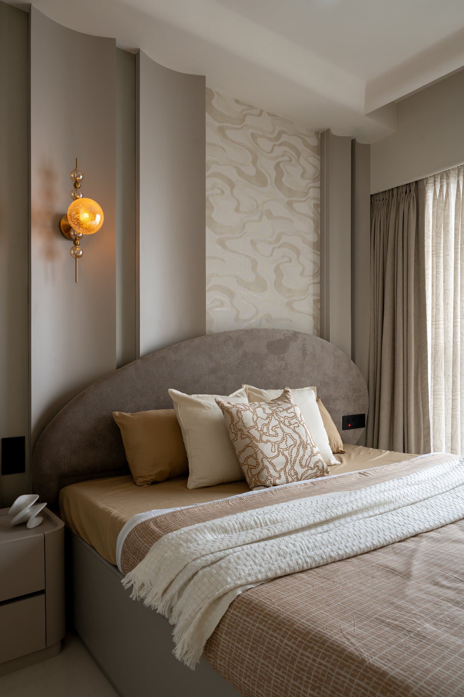 A second bedroom, where fluted vertical panels frame a curved upholstered headboard and a wavy printed panel