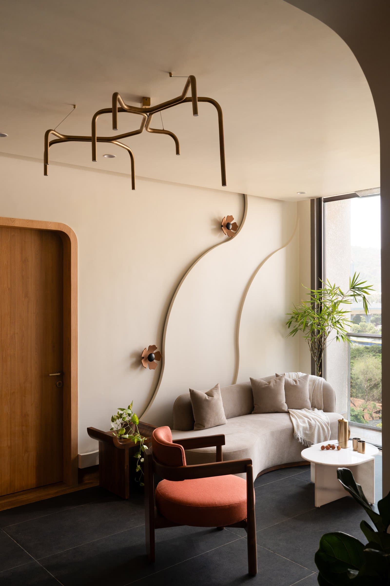 The living room, where a branching brass-toned ceiling fixture and ribbon-like wall relief establish the home's sculptural language